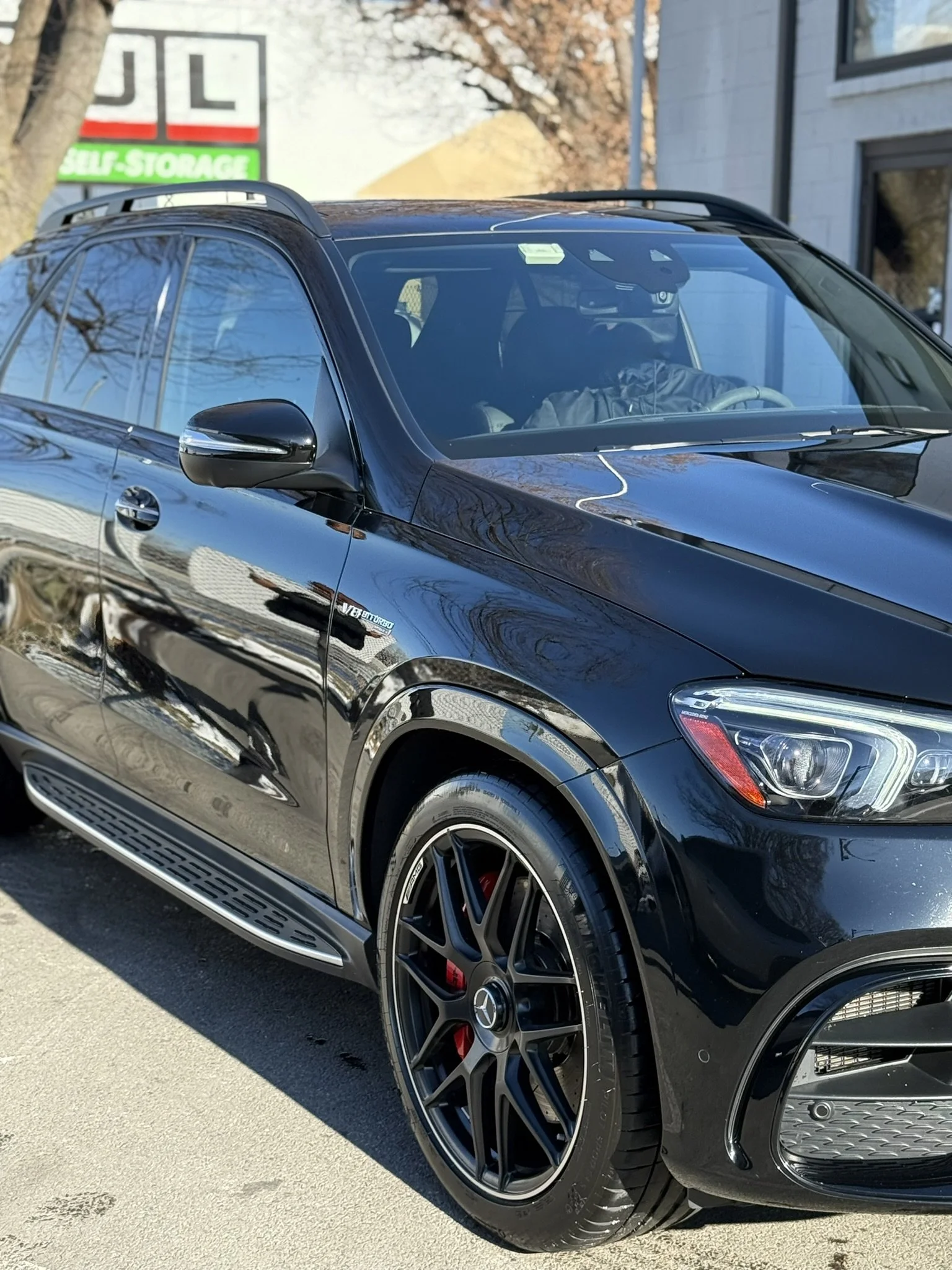 A black Mercedes-Benz SUV parked on the street with reflective paint and sporty black rims.