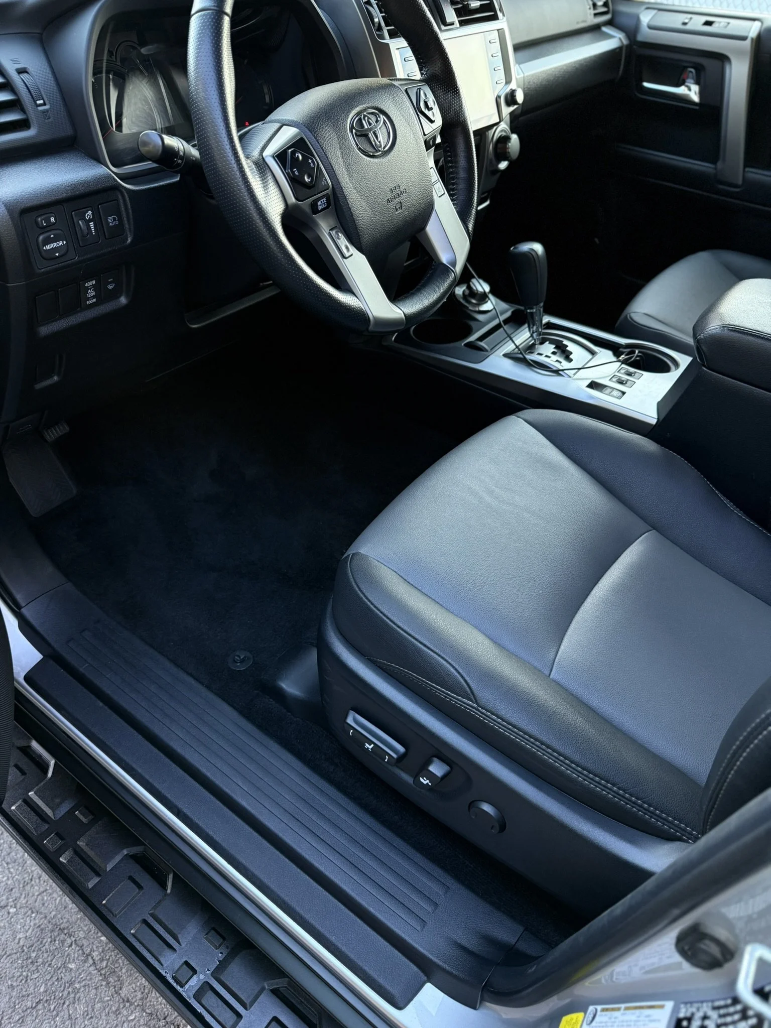Interior of a Toyota vehicle, showing black leather seats, a steering wheel, gear shift, and dashboard with an infotainment screen.