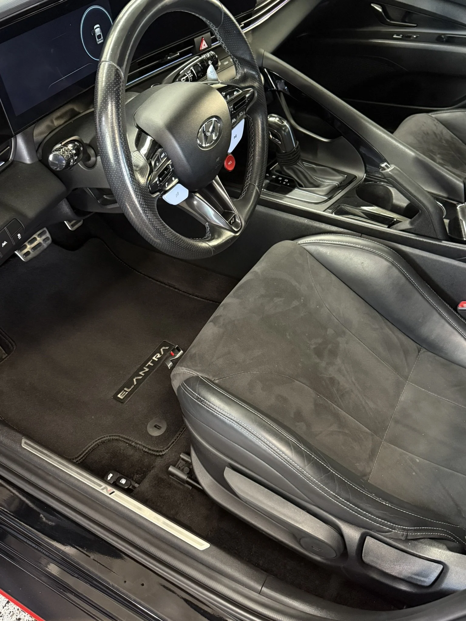 Interior of a Hyundai Elantra car showing the steering wheel, dashboard, gear shift, driver's seat, and floor mat.