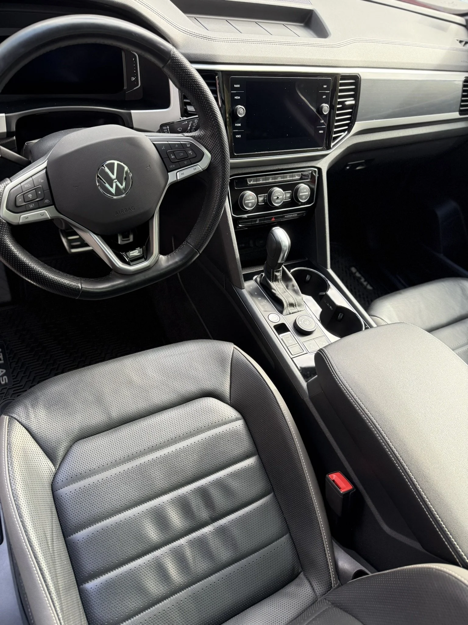 Interior view of a vehicle showing the steering wheel with a Volkswagen logo, a center console with a gear shifter, and an infotainment screen on the dashboard.