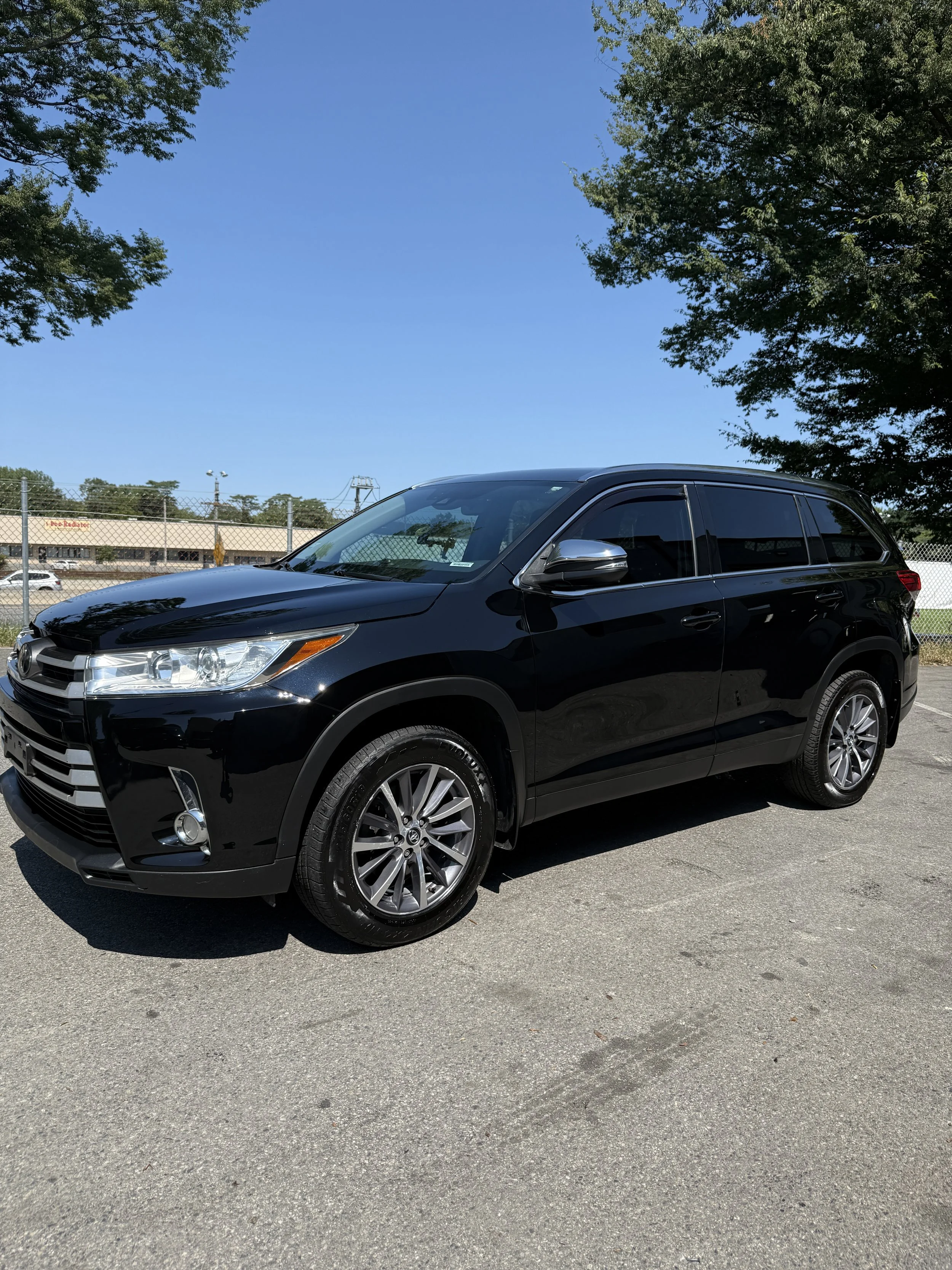 Black SUV parked in a parking lot with trees and a blue sky in the background.