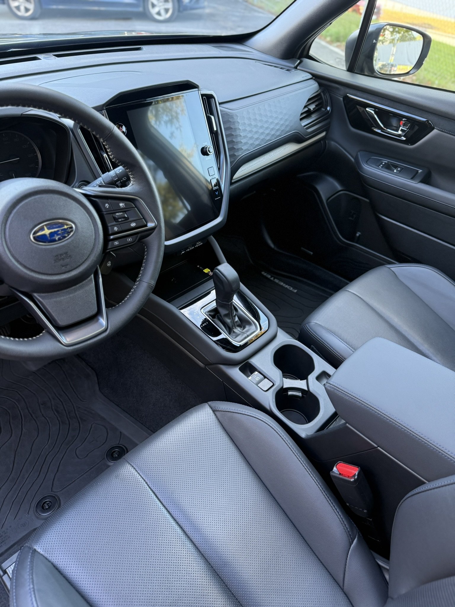 Interior of a modern car showing the steering wheel, digital dashboard, gear shifter, and center console with cup holders.