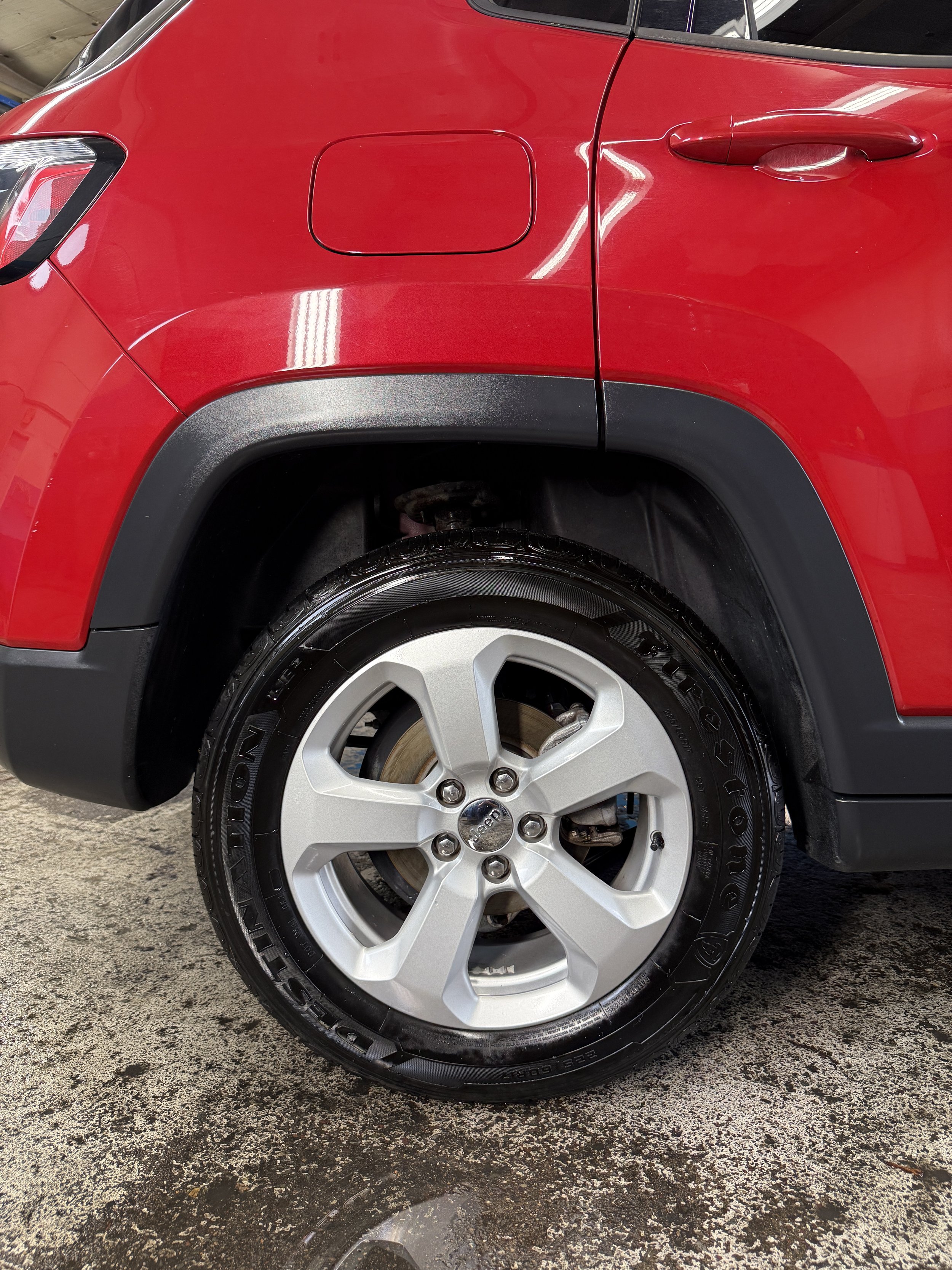 Close-up of a red car's front wheel and part of the front body, with a black tire, silver rim, and visible brake components.
