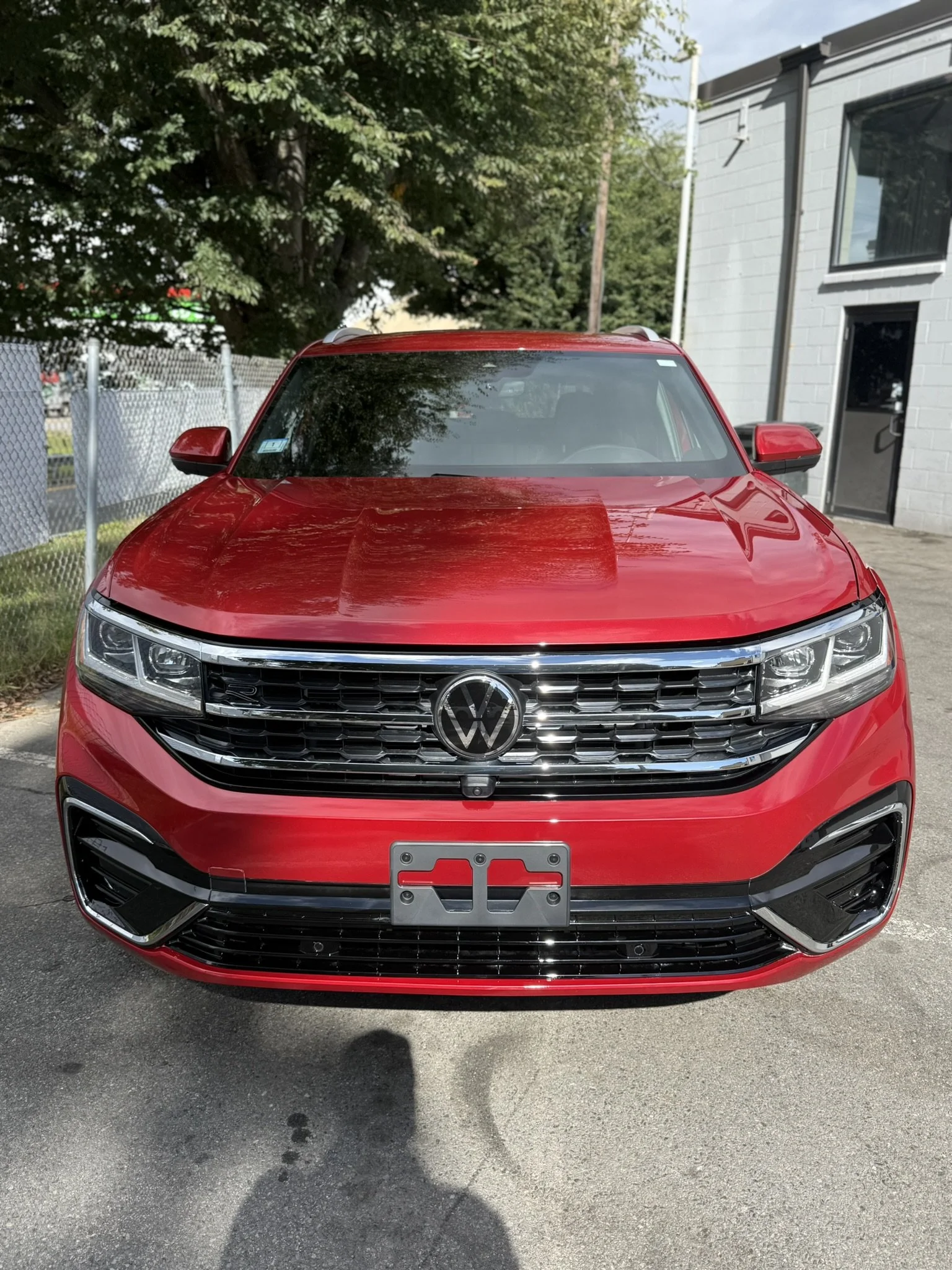 Front view of a red Volkswagen sedan parked outdoors on pavement, with a building and trees in the background.