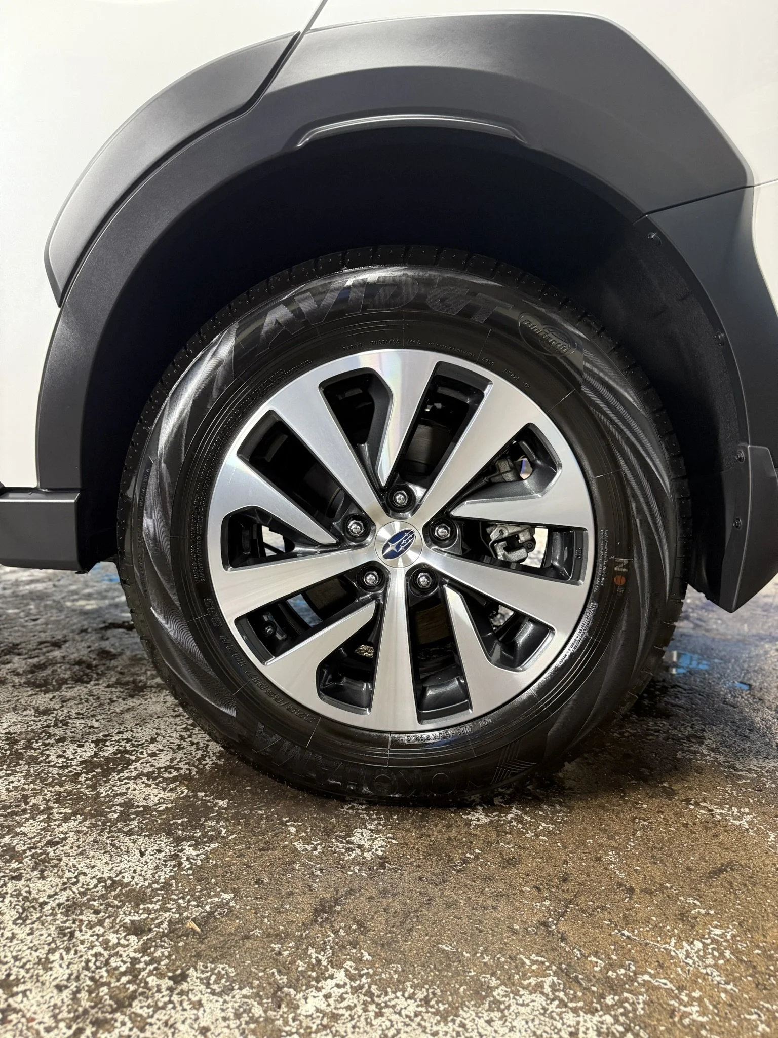 Close-up of a car's front wheel with a metallic rim and black tire, parked on a textured surface.
