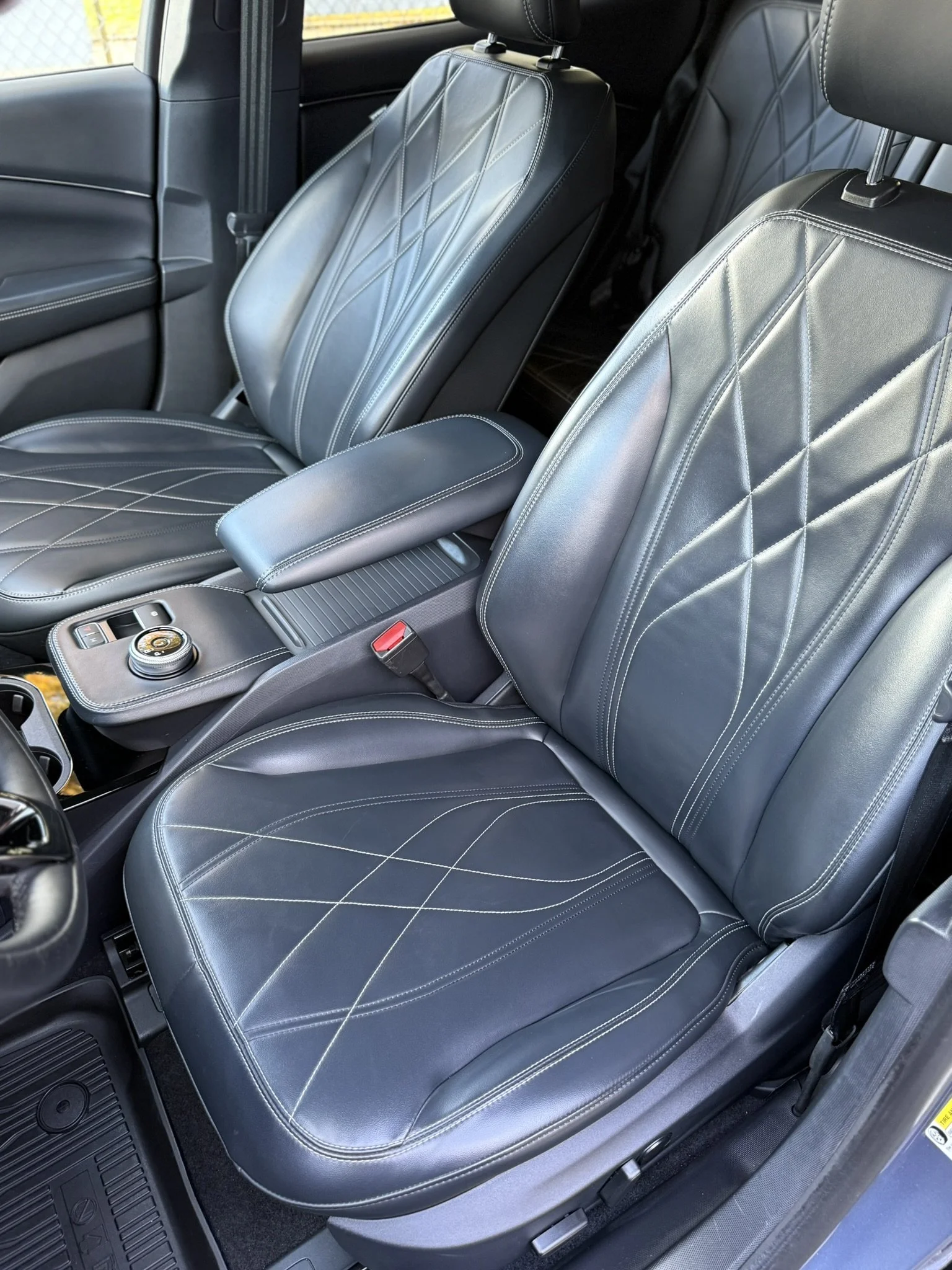 Front seats of a vehicle with black leather upholstery and white stitching, center console with controls and armrest.