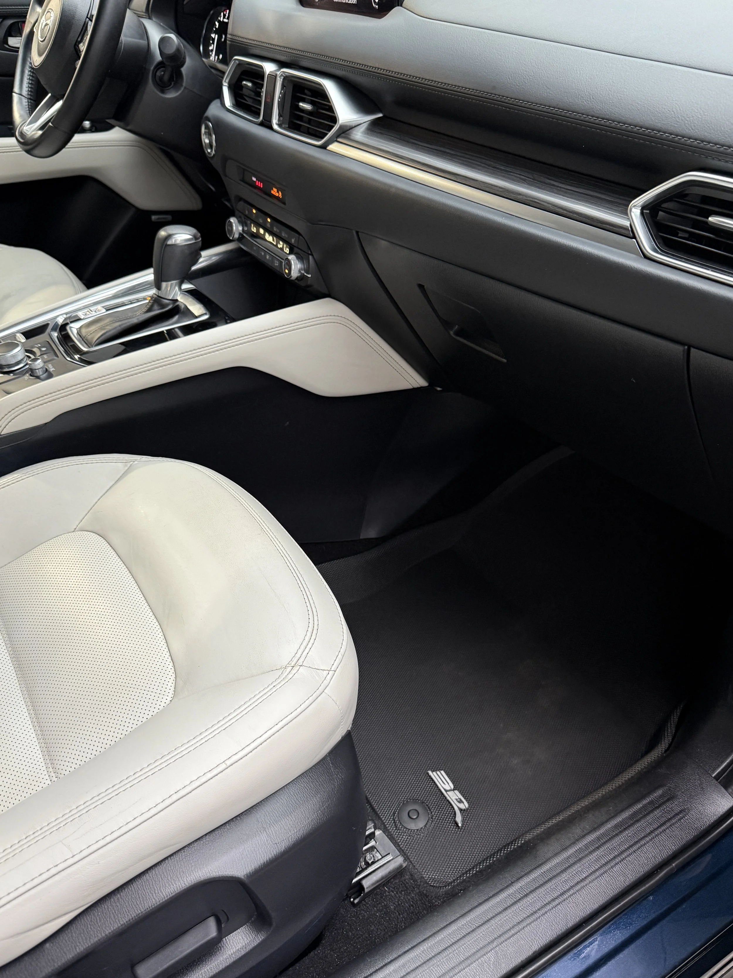 Interior of a car showing a gear shift, control knobs, black and cream-colored seats, and a floor mat with 