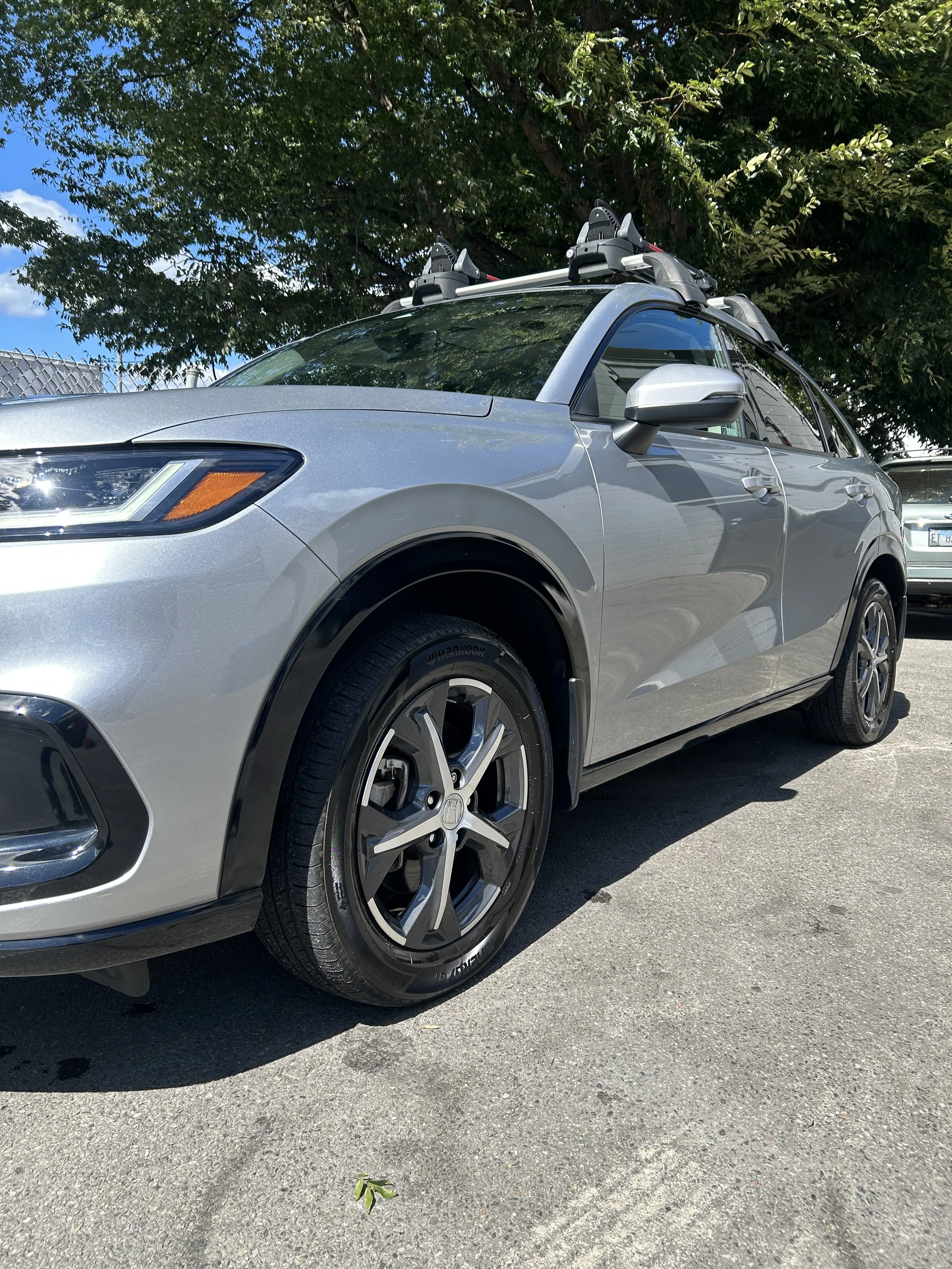 Silver Honda SUV parked outdoors on a paved surface, with a tree and another vehicle in the background.