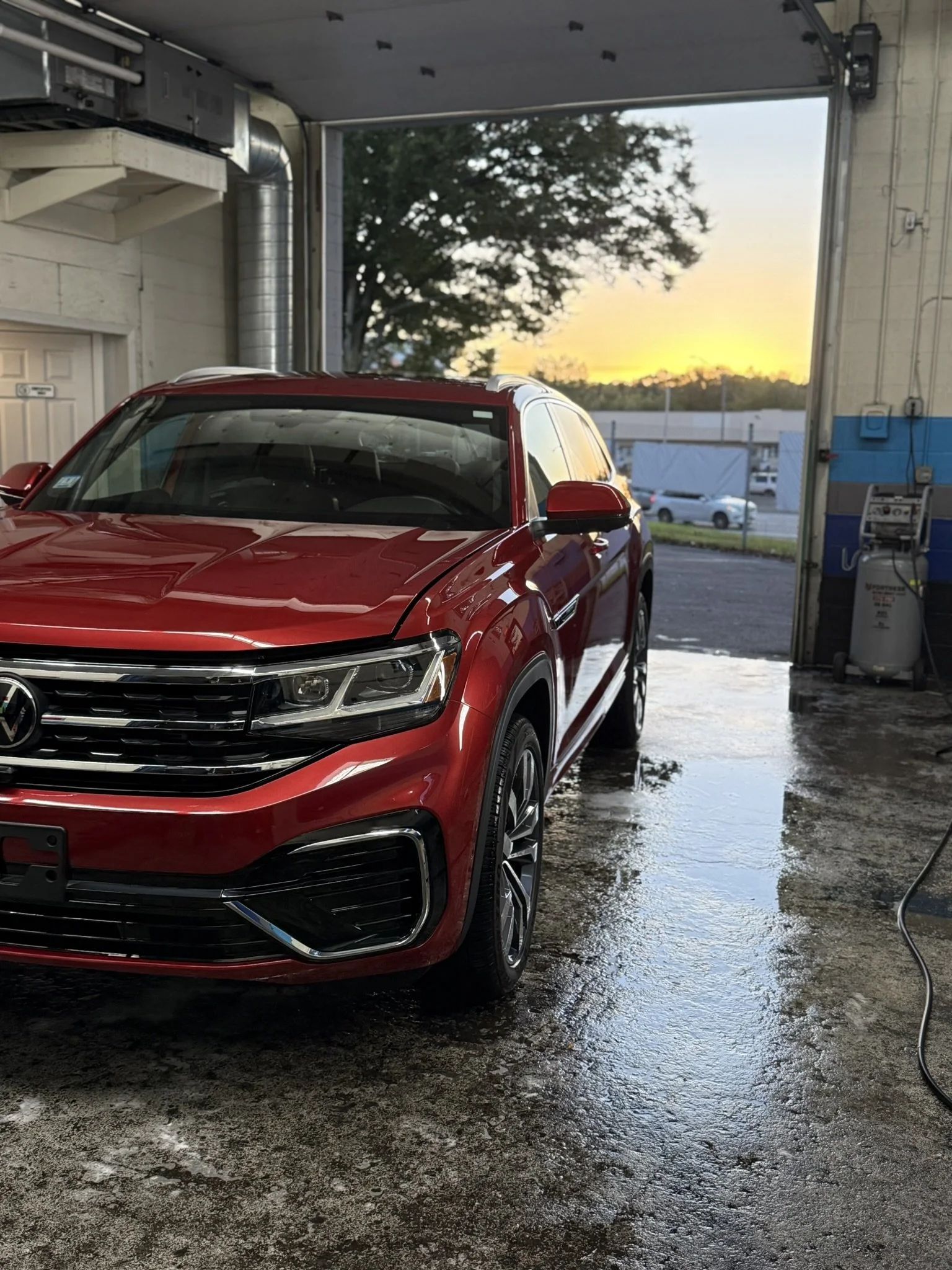 Red Volkswagen SUV inside an automatic car wash bay with a sunset view outside.