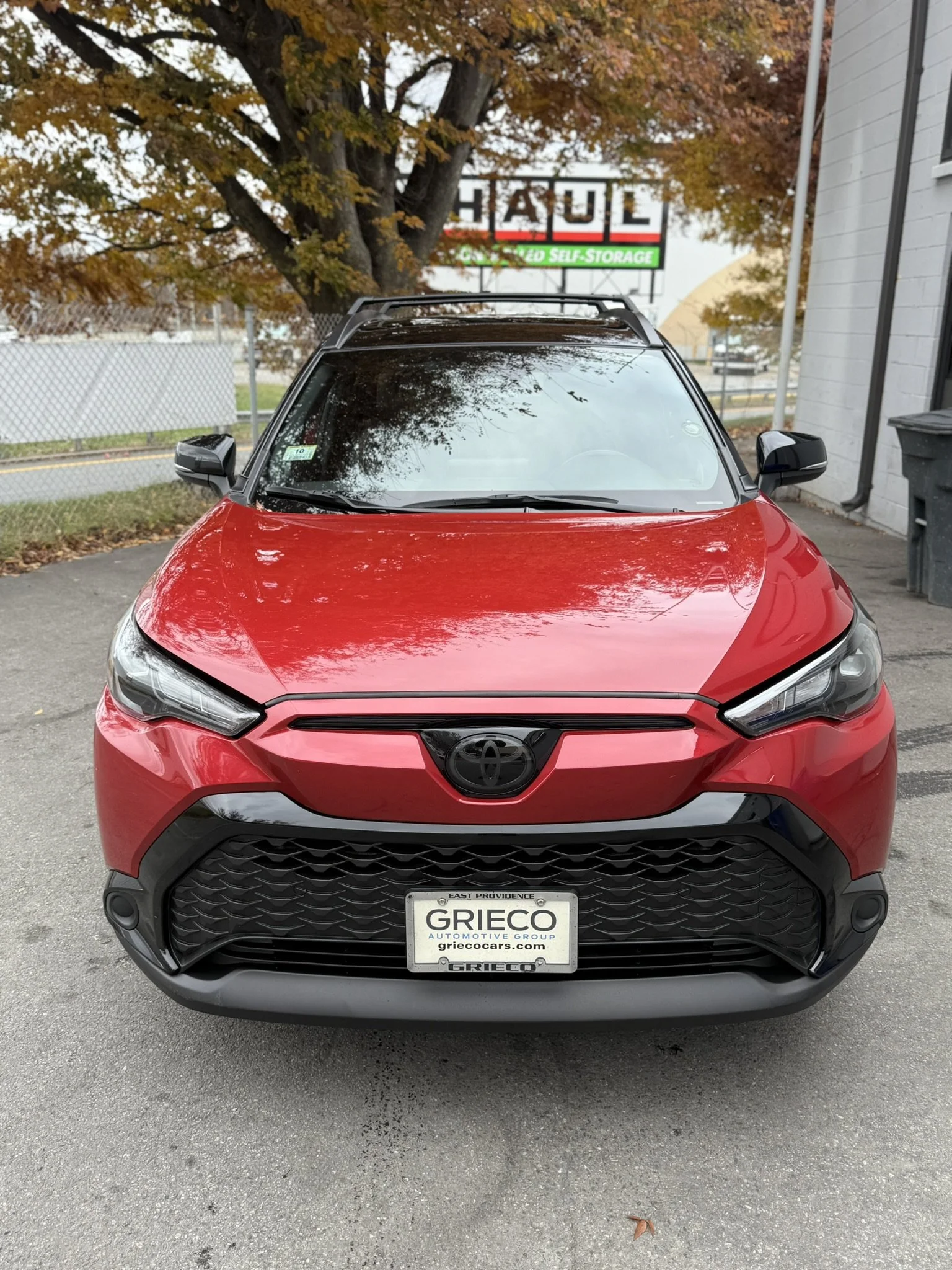 Front view of a red Toyota SUV parked in a lot, with autumn trees and a self-storage sign in the background.