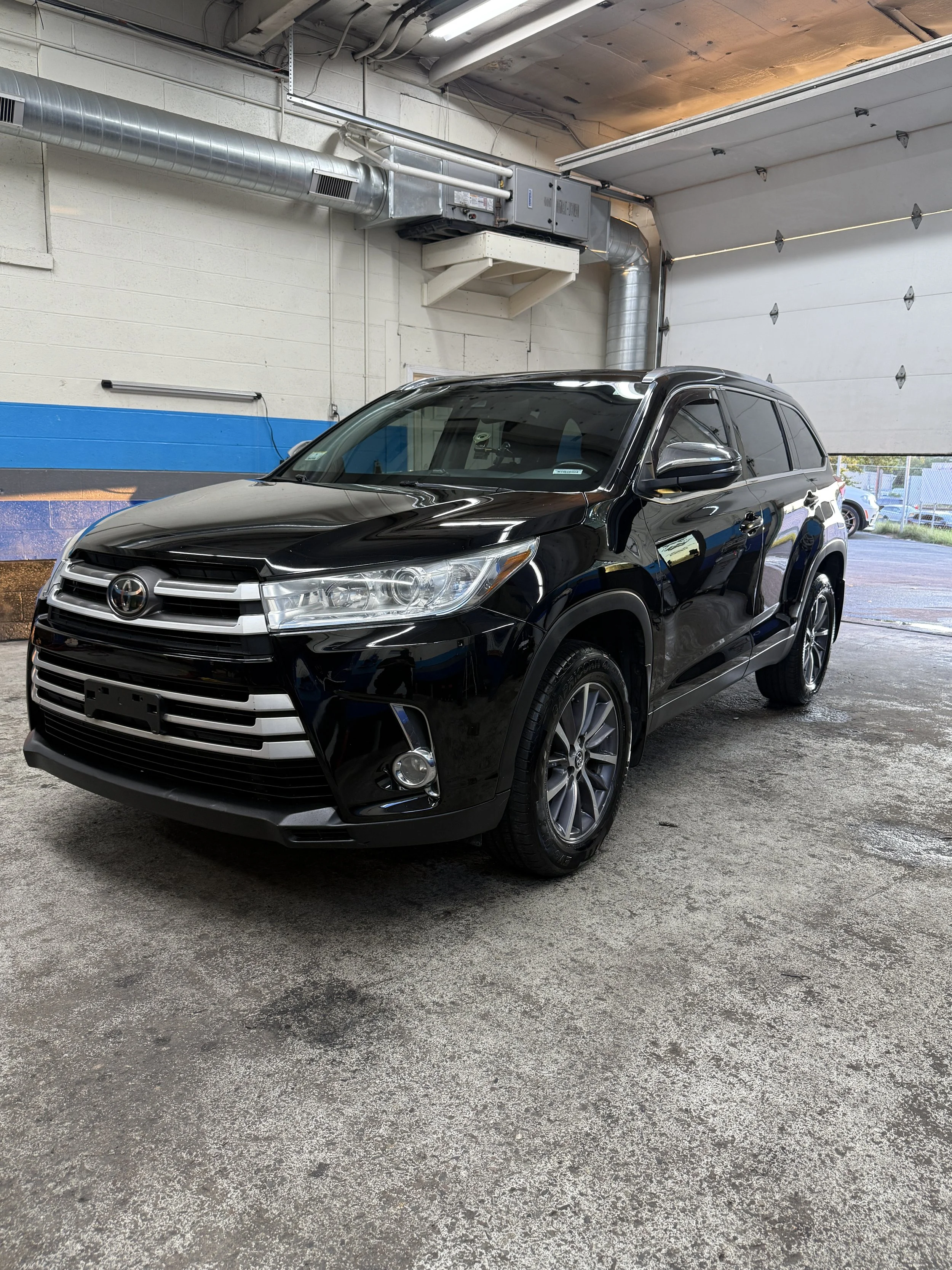 Black Toyota SUV parked inside a garage with an industrial ceiling, including visible ductwork and ventilation pipes.