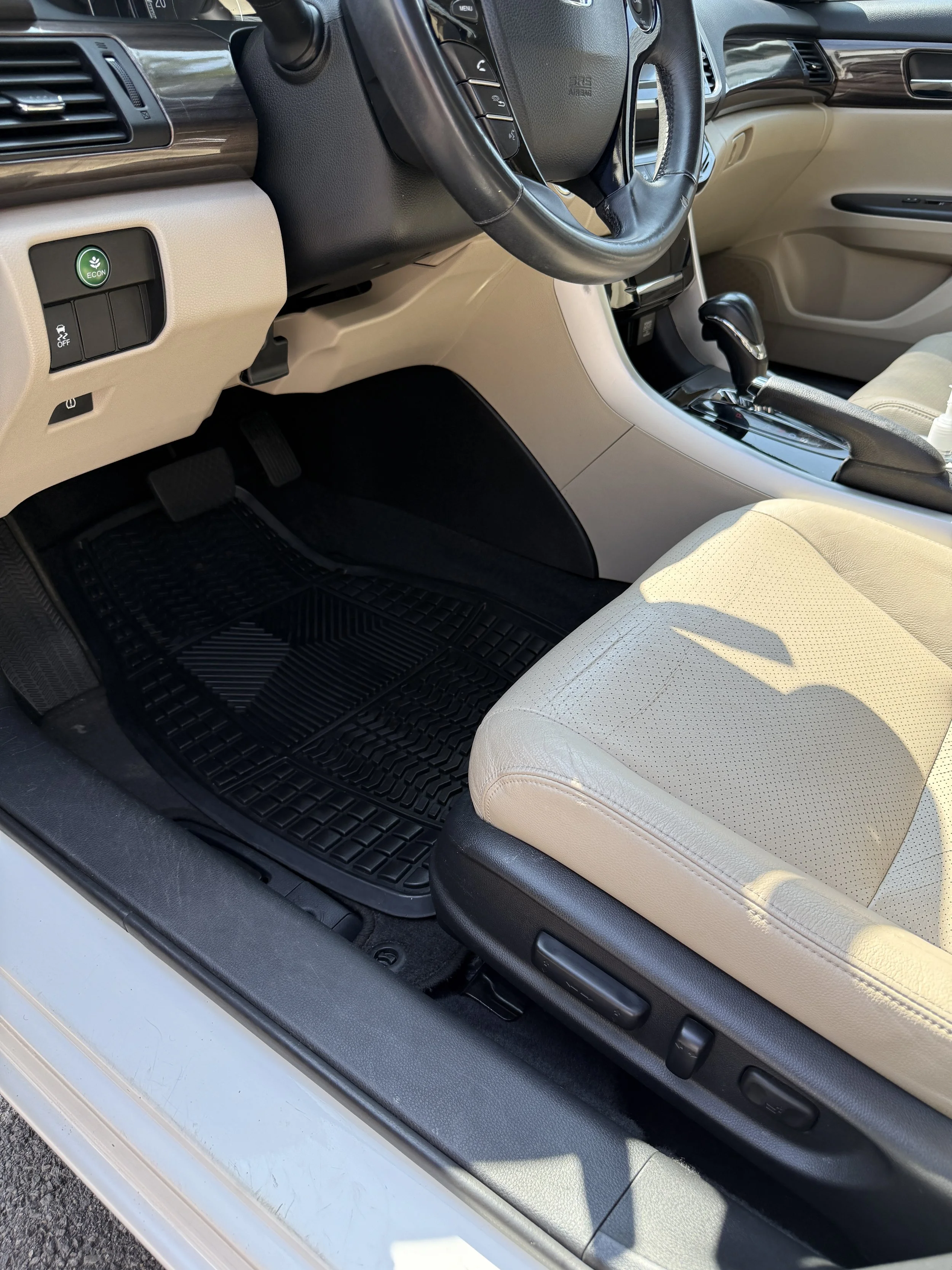 Interior of a car showing the driver's seat, steering wheel, gear shift, and dashboard with beige and black finishes.