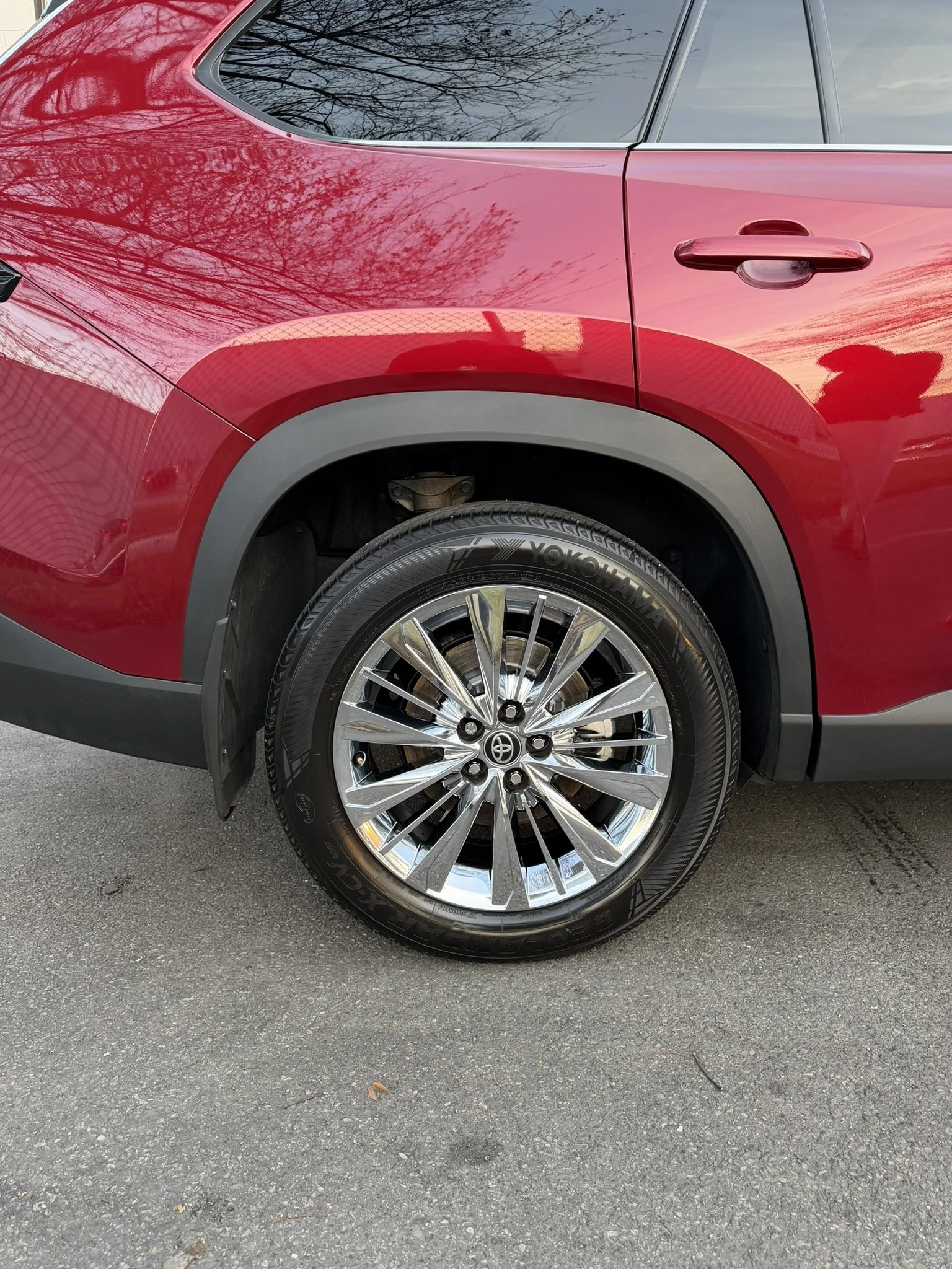 Close-up of a red SUV showing the front right wheel with a chrome rim, Yokohama tire, and a portion of the body with reflections of trees and sky.