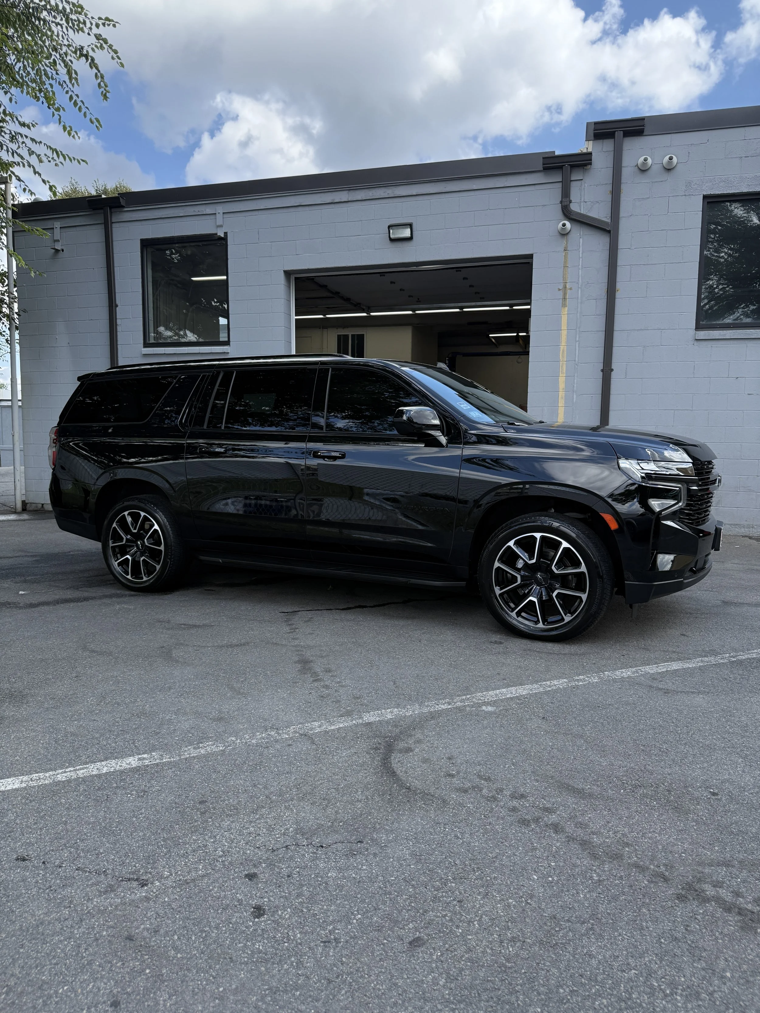 Black SUV parked outside in a parking lot with a gray industrial building in the background, partly cloudy sky overhead.