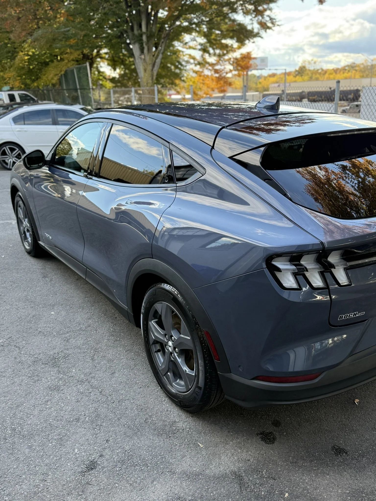 A blue electric SUV parked in a parking lot with trees and other vehicles in the background.