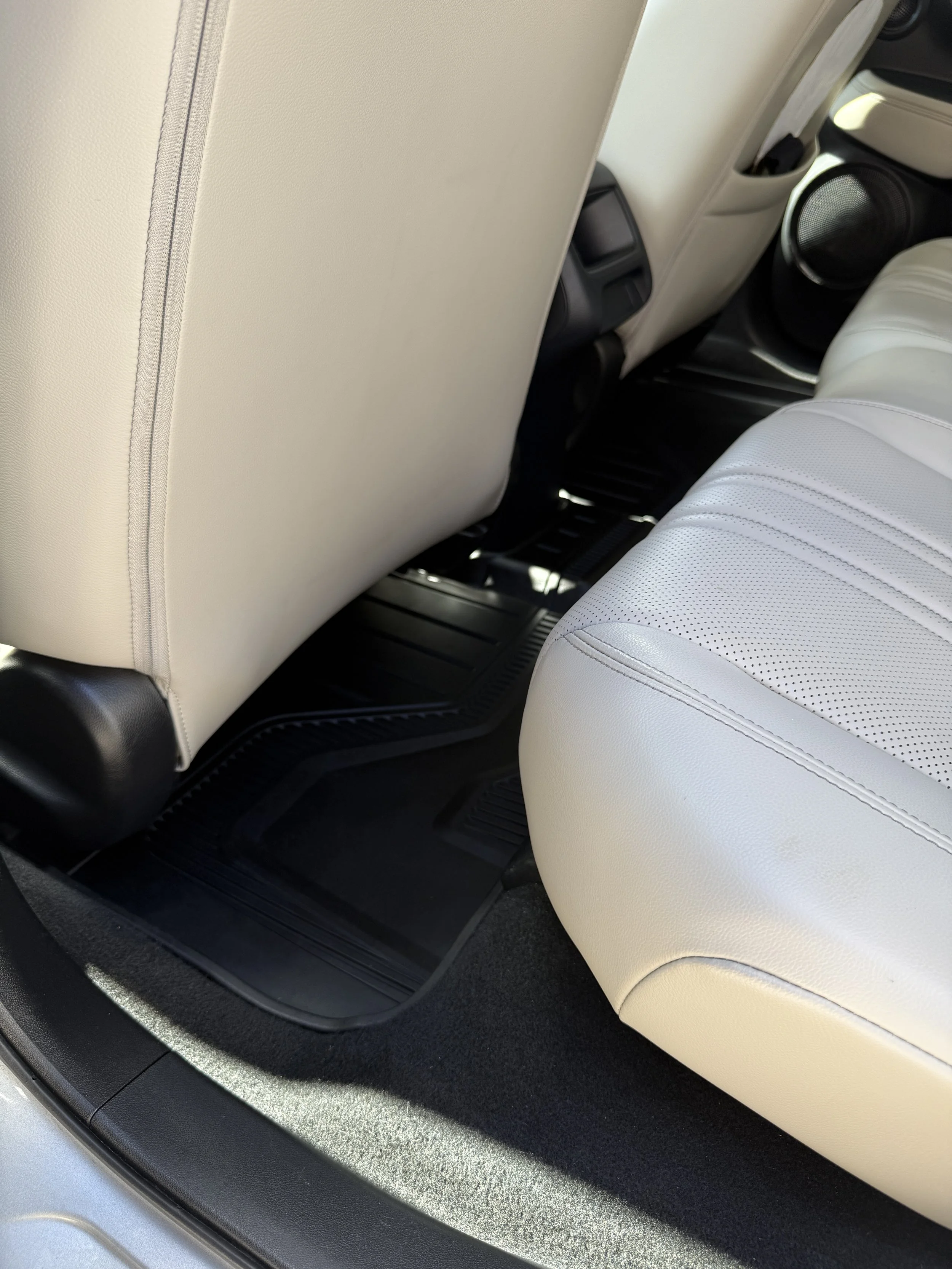 Interior of a vehicle showing the back of the front seats, the rear seat, and floor mats.