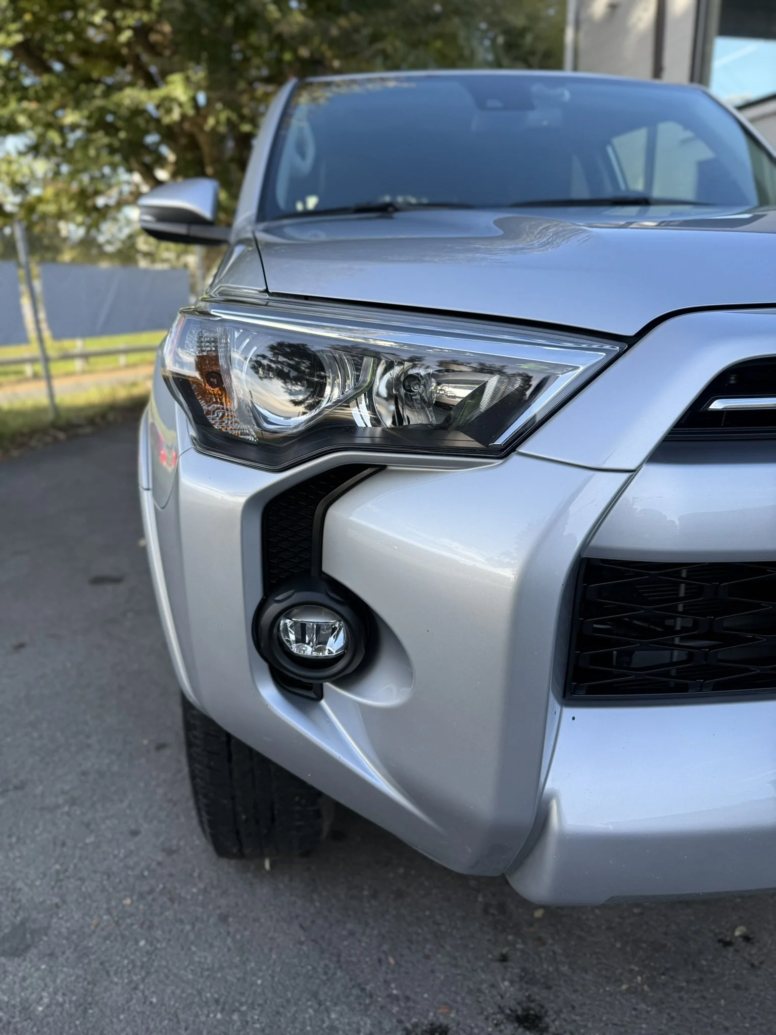 Close-up of the front left side of a silver SUV, including the headlight, fog light, and part of the front grille, parked outdoors.