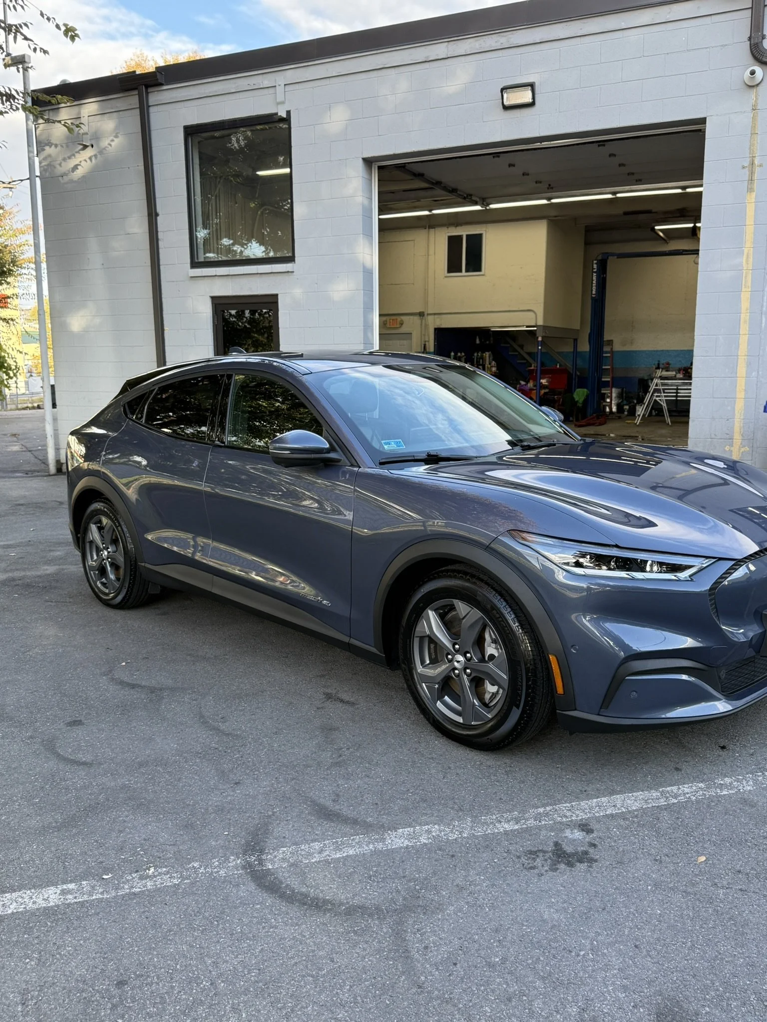 A blue modern car parked outside a white building with a large garage door open, revealing a workshop inside.