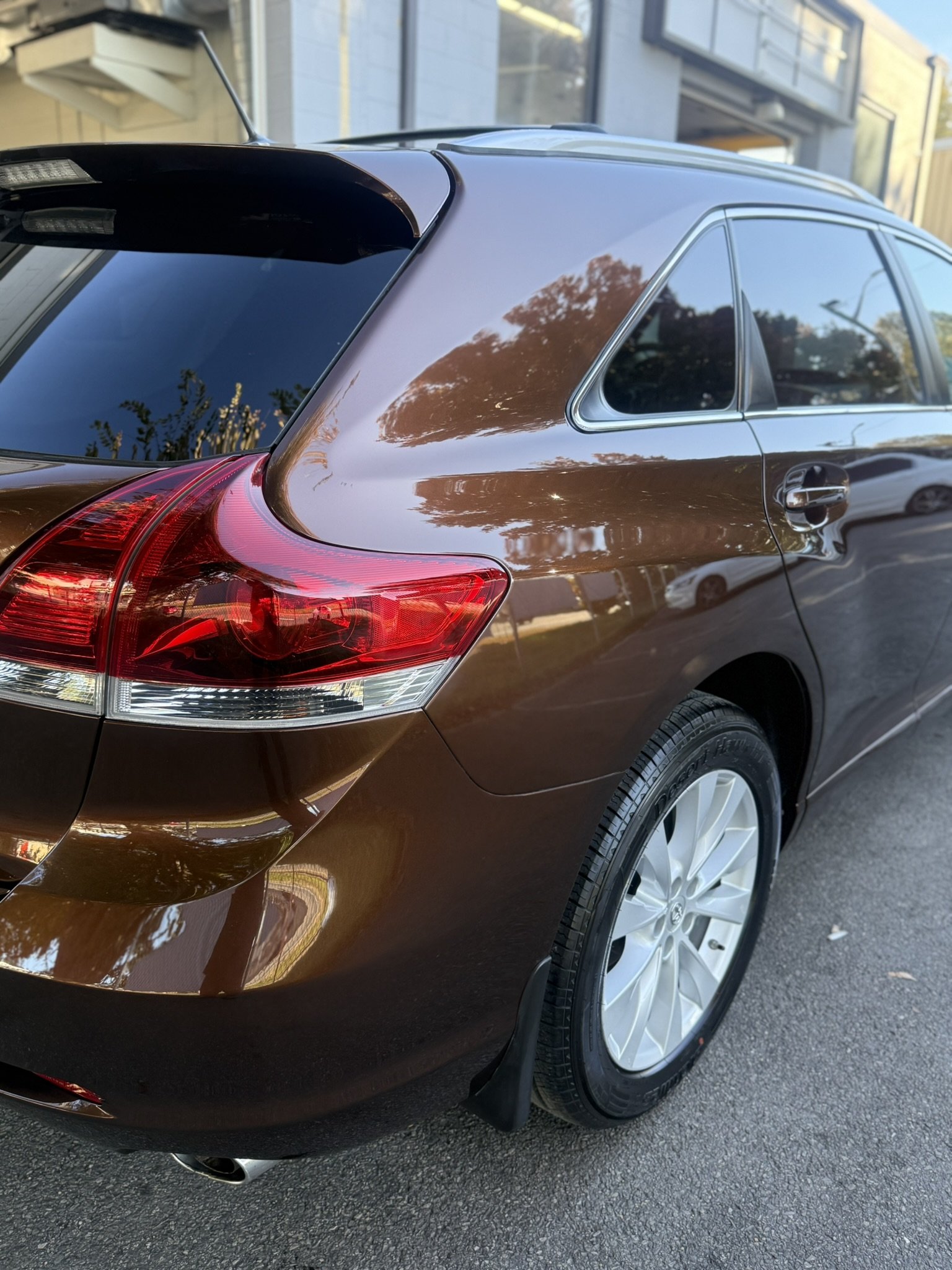 Close-up of a brown station wagon showing the rear left side, including the tail light, rear window, and a portion of the wheel with a tire.