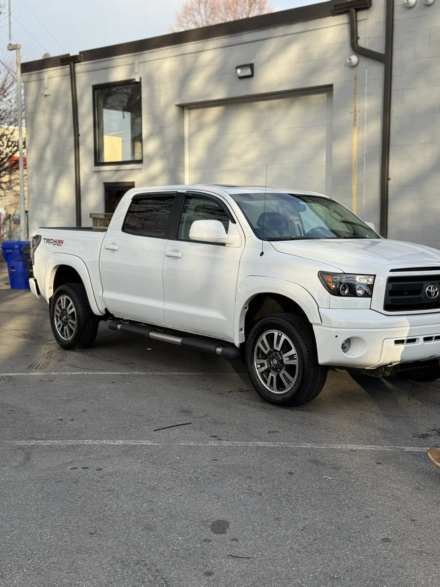 A white Toyota pickup truck parked in a parking lot near a modern building during daylight.