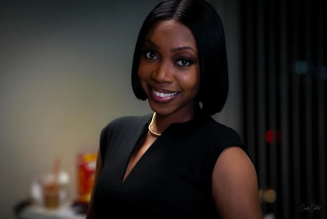 A woman with a shoulder-length black bob haircut smiling and wearing a black sleeveless top and a thin gold necklace.