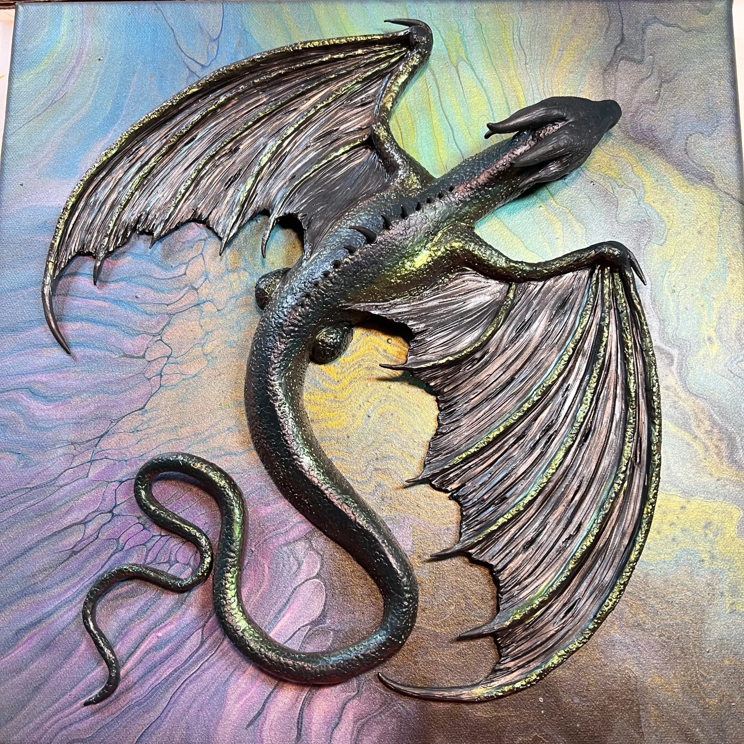 A detailed sculptural depiction of a dragon with large, textured wings and a long, curved tail, set against a colorful, swirling background.
