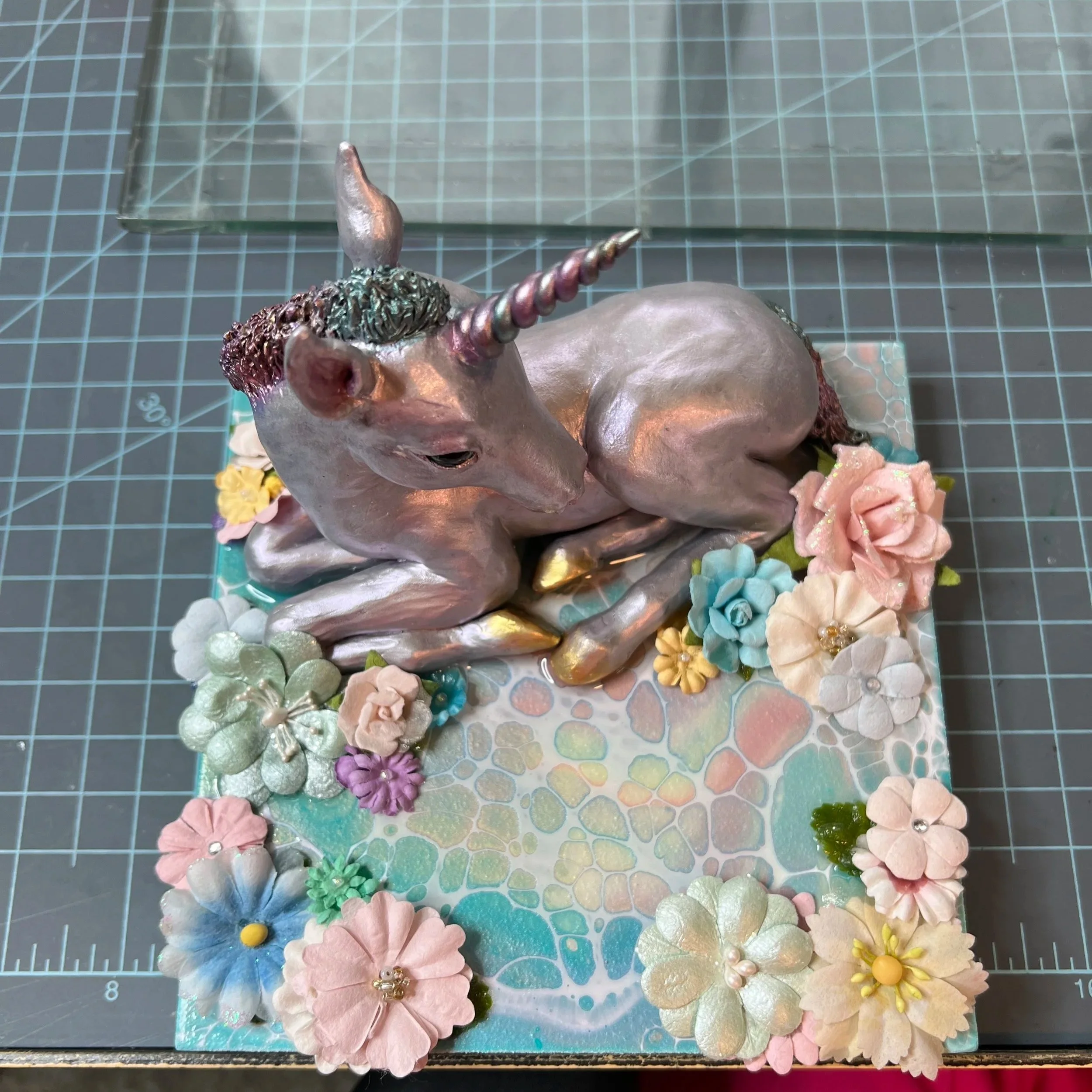 A decorative unicorn figurine with a pink body, metallic horn, and a flowered base with pastel-colored flowers.