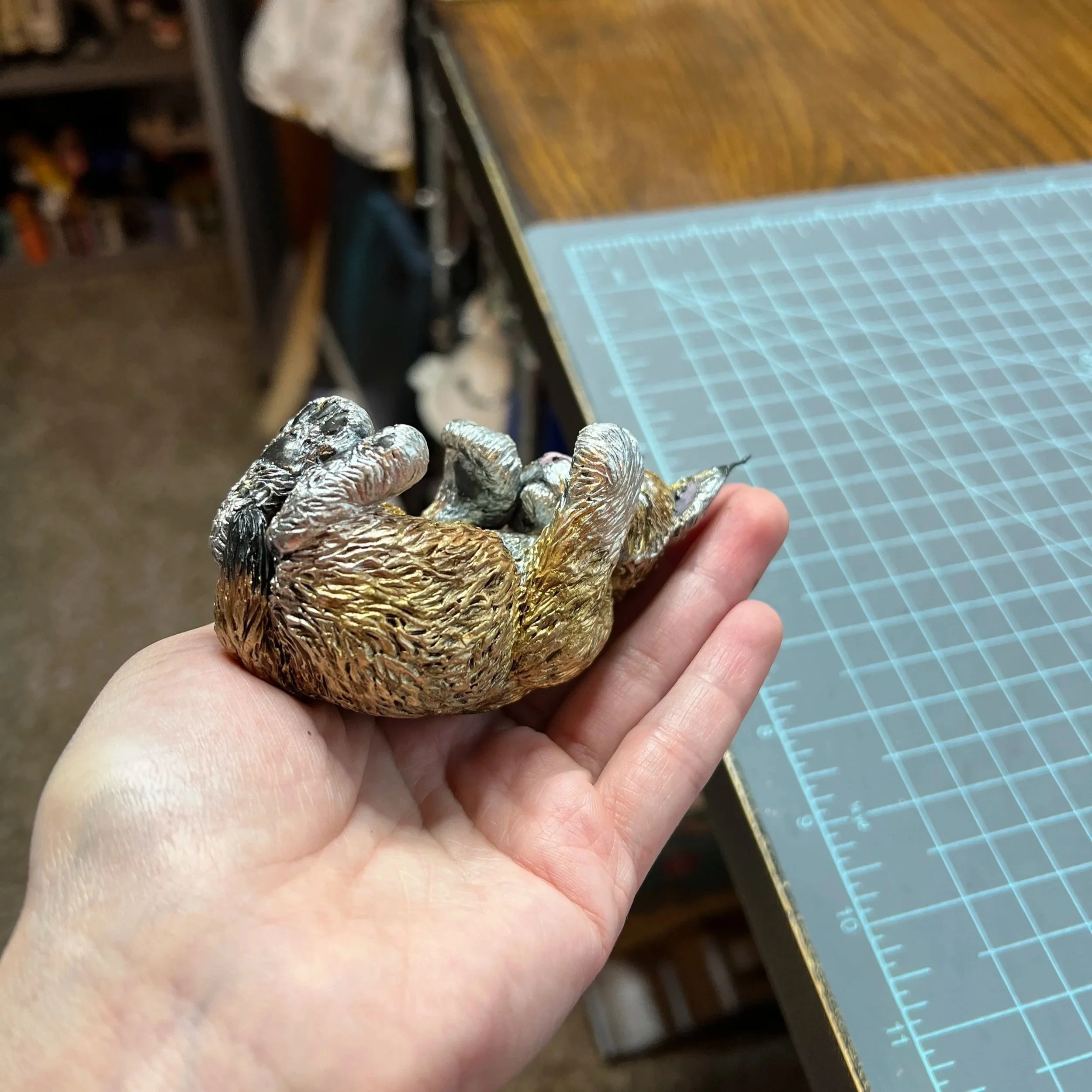 A hand holding a small, detailed, metallic sculpture of a lynx kitten with a shiny, textured surface.