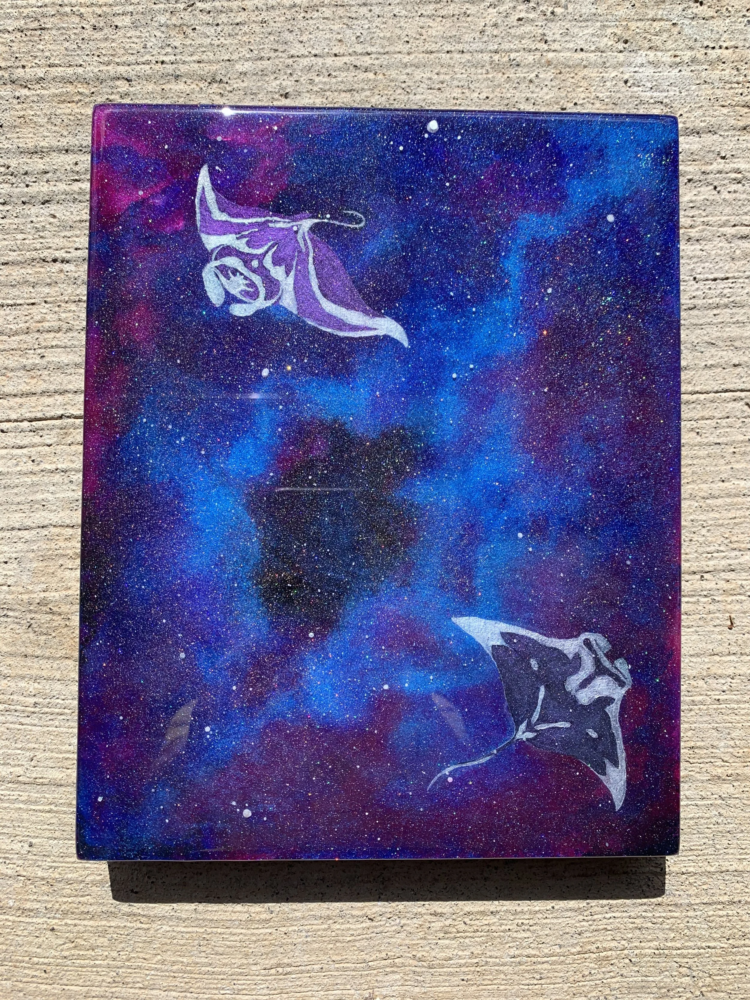 A painting of a colorful galaxy with a purple and blue nebula, featuring two white and black manta rays flying in opposite directions.