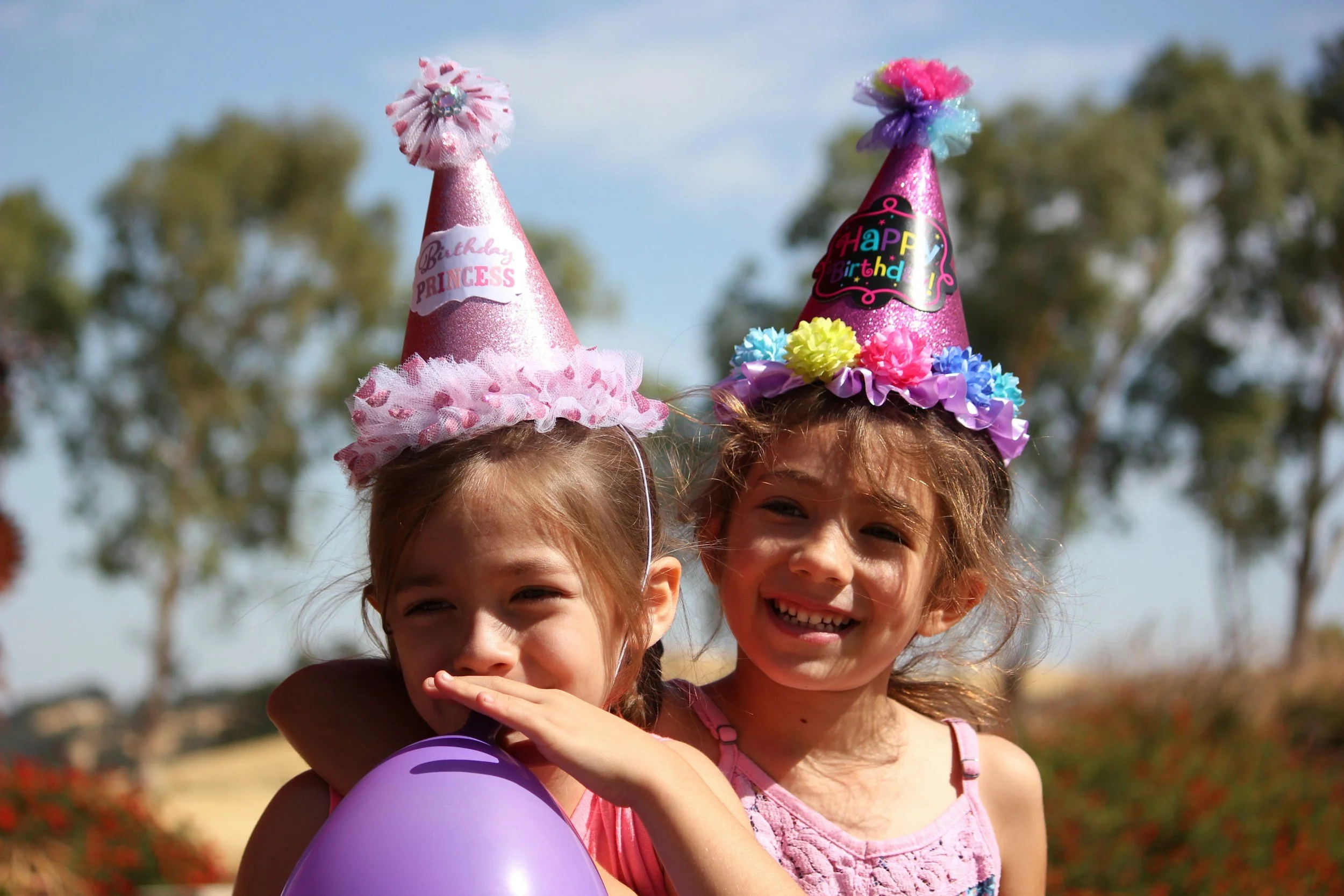 Two young girls wearing birthday party hats, one pink with