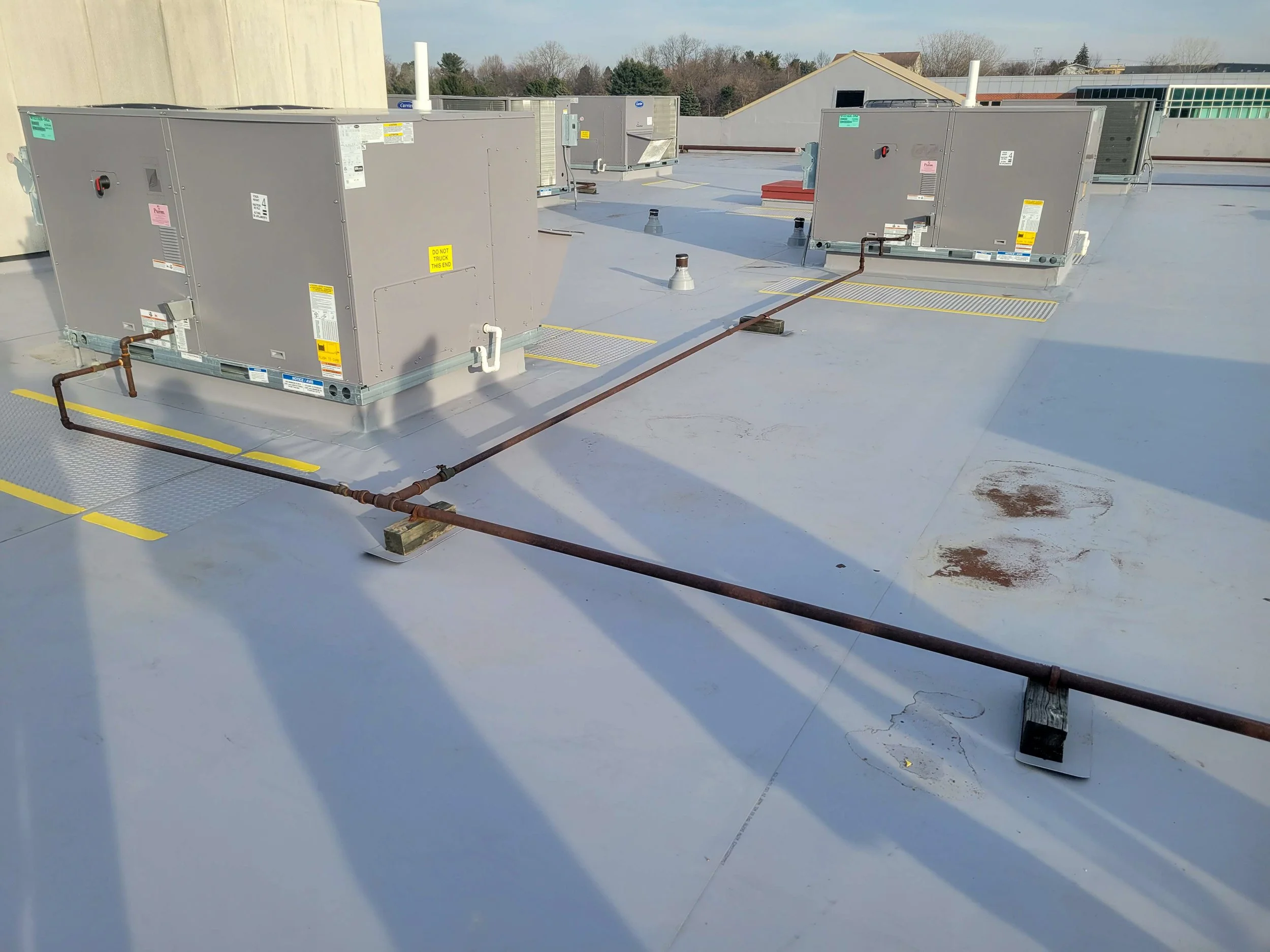 Rooftop with multiple HVAC units and a rusty pipe running across the flat surface.