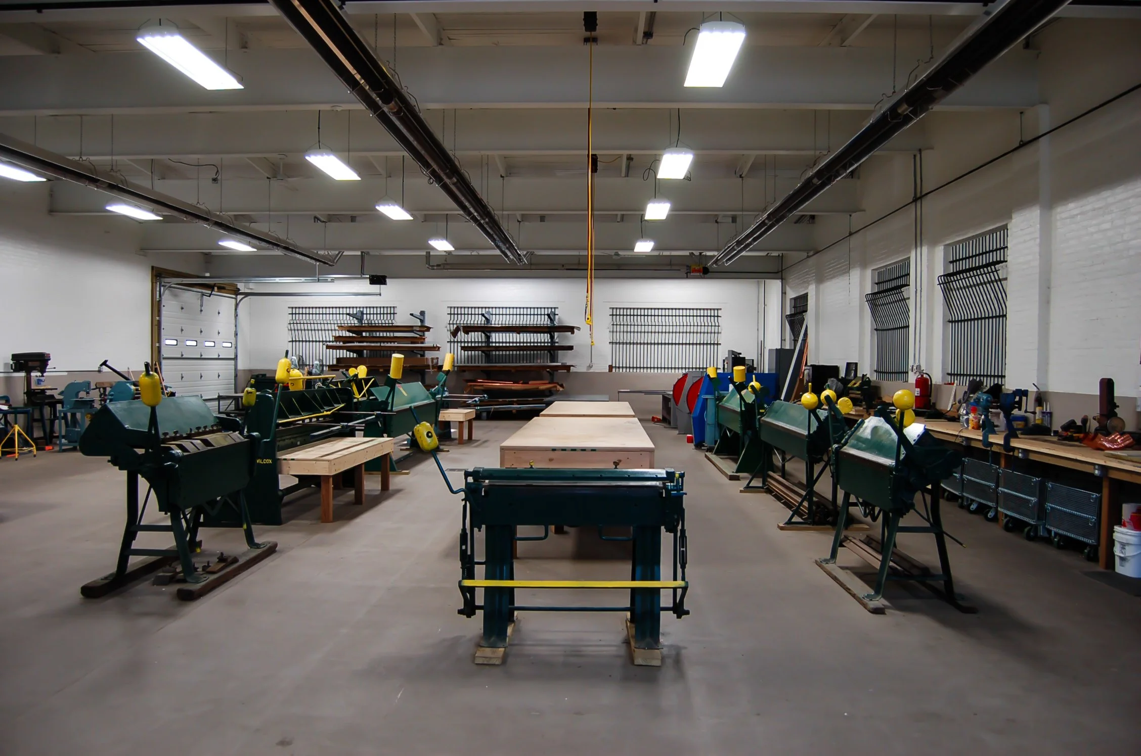 An empty woodworking workshop with various power tools, workbenches, and shelves, well-lit with bright ceiling lights.