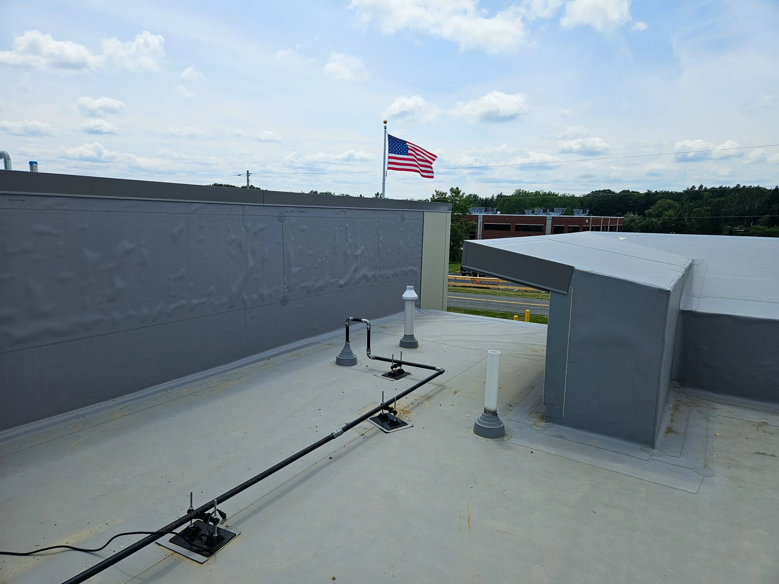 Rooftop with vents and pipes under a cloudy sky, American flag waving in the background.