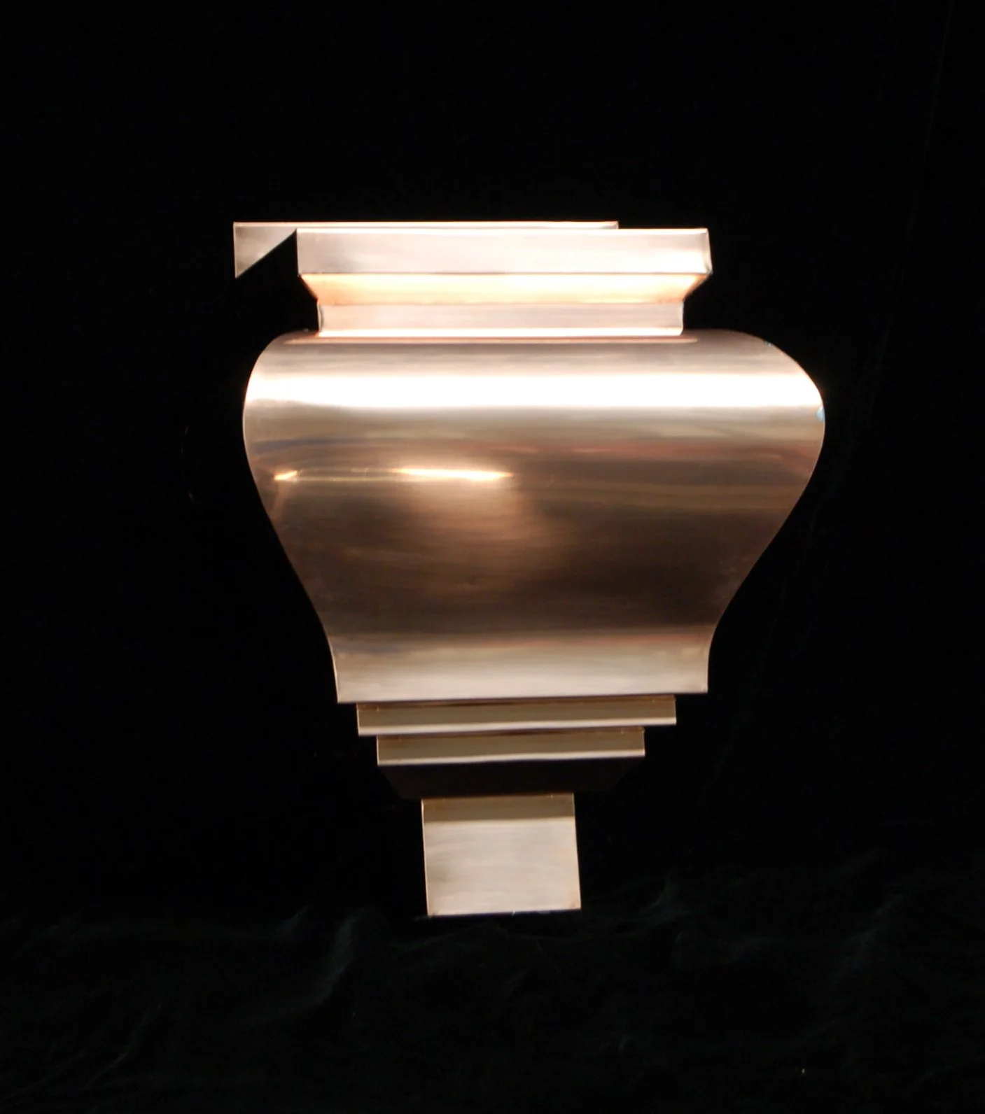 A metallic vase sculpture with a reflective surface, set against a black background.
