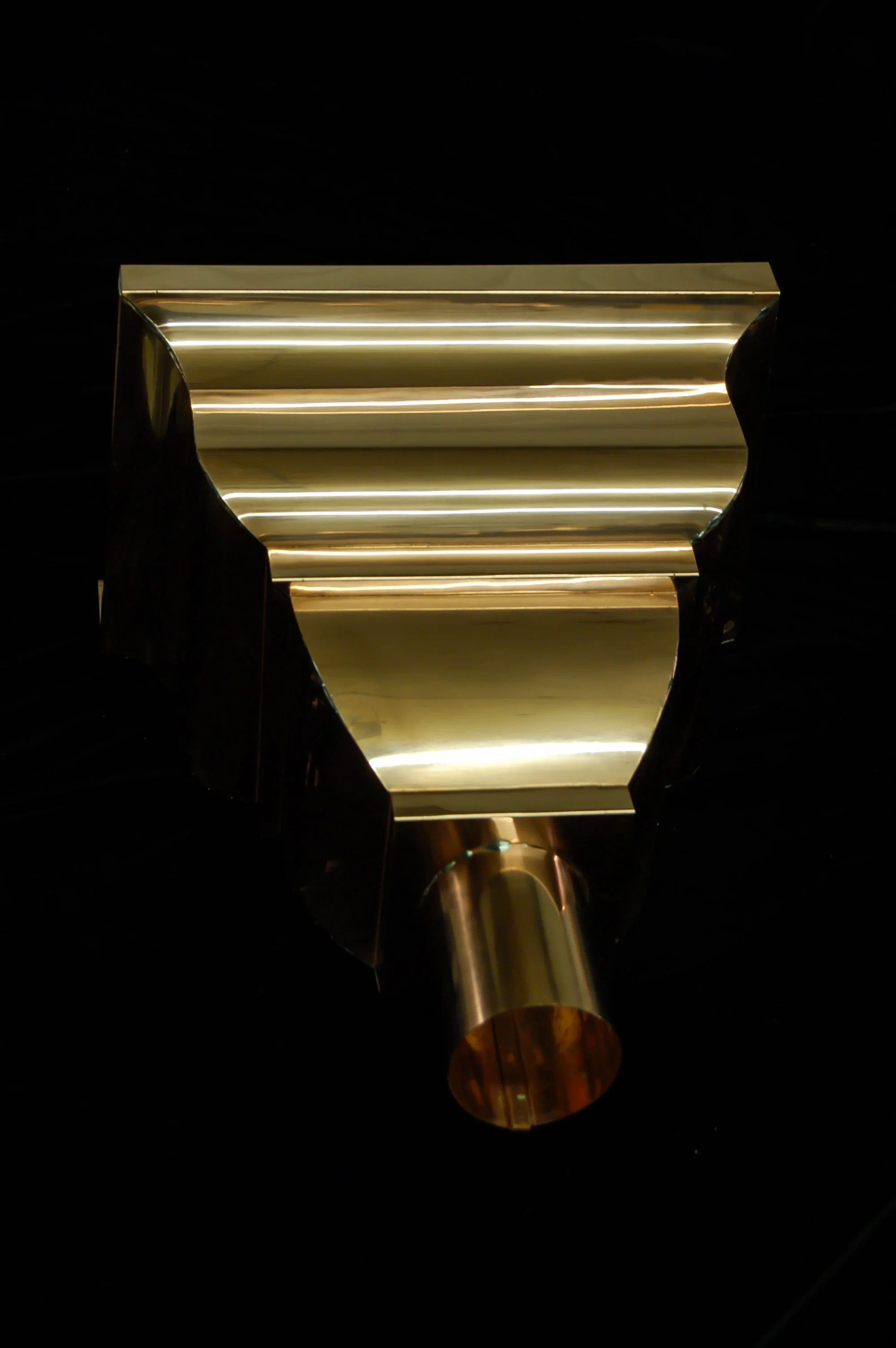 A metallic object with gold and silver tones against a black background, featuring a cylindrical handle and a rectangular body with rounded edges.