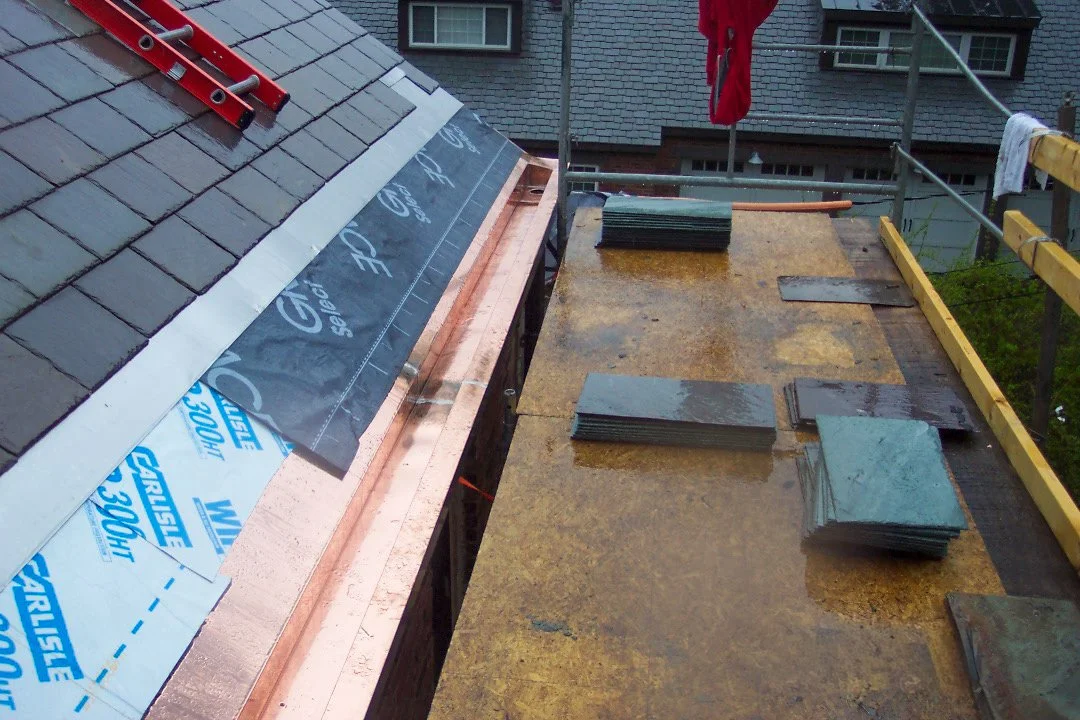 Roof construction site showing slate tiles, roofing underlayment, and building materials on a scaffolded roof.