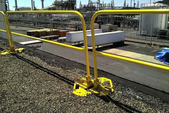Yellow safety guardrails on a rooftop overlooking industrial rail tracks and storage containers at an industrial facility.