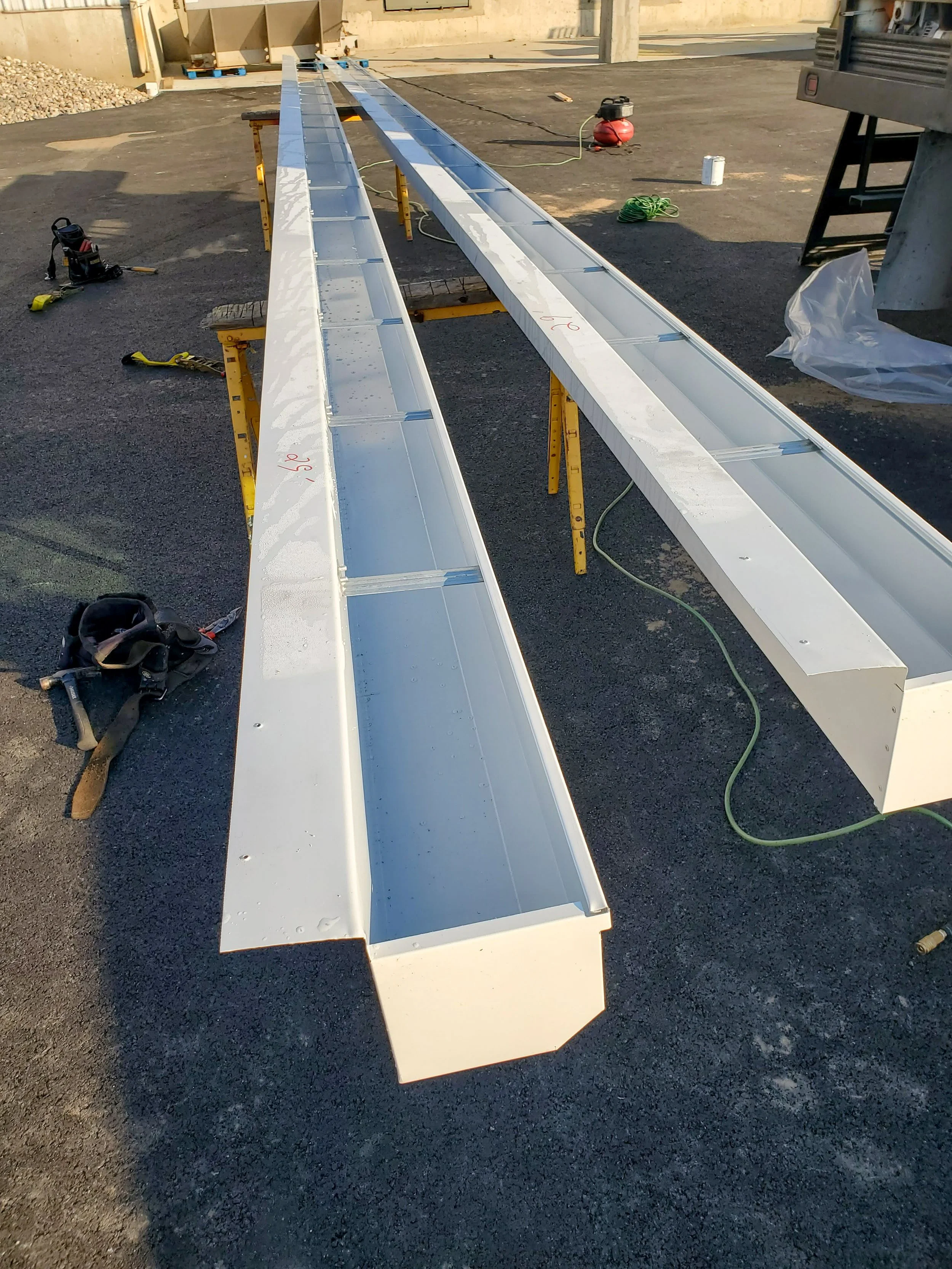 Construction site with two long, white metal beams supported on yellow sawhorses, some tools and electrical cords scattered around.