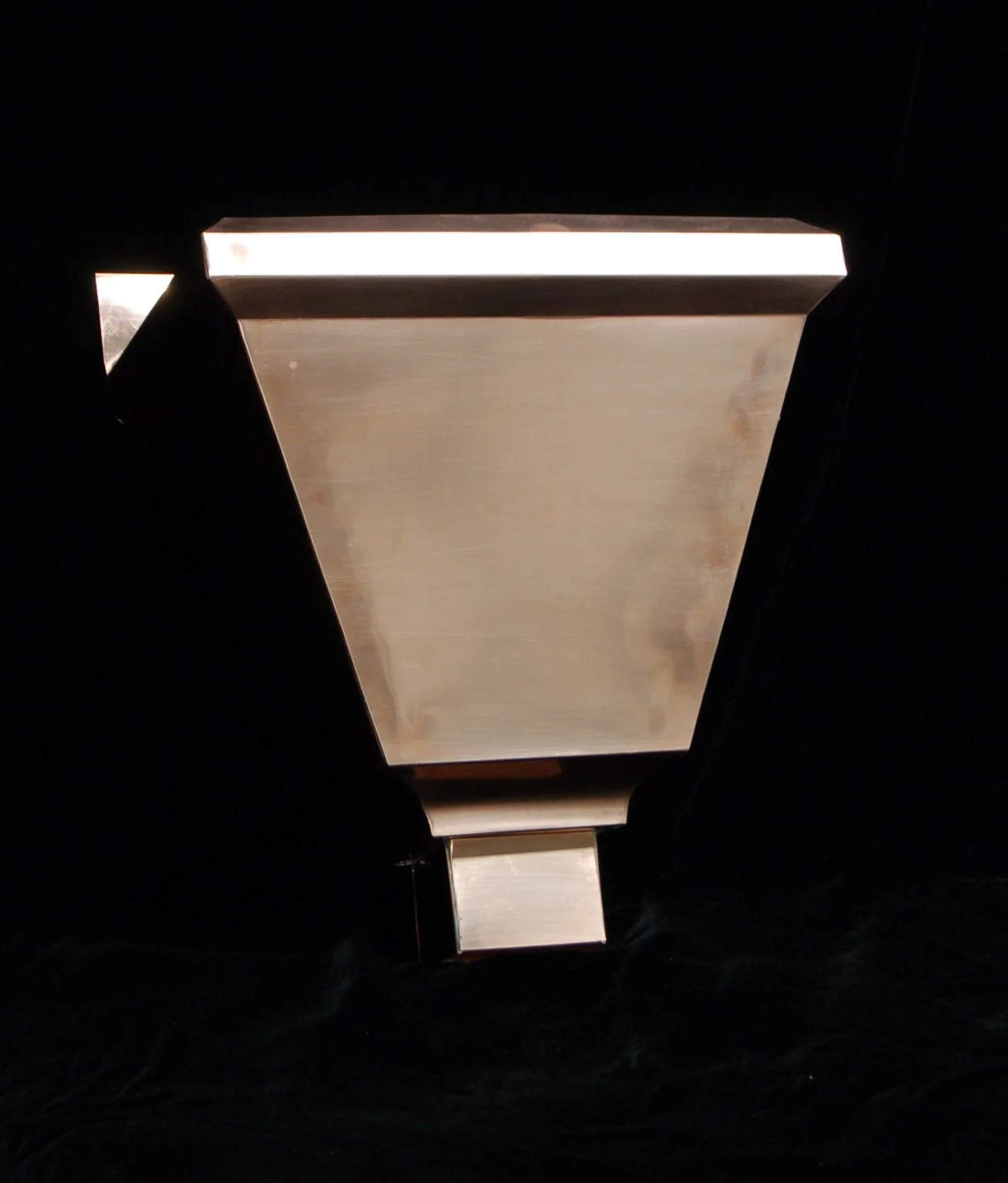 A metallic outdoor lamp with a rectangular shape, mounted against a black background.