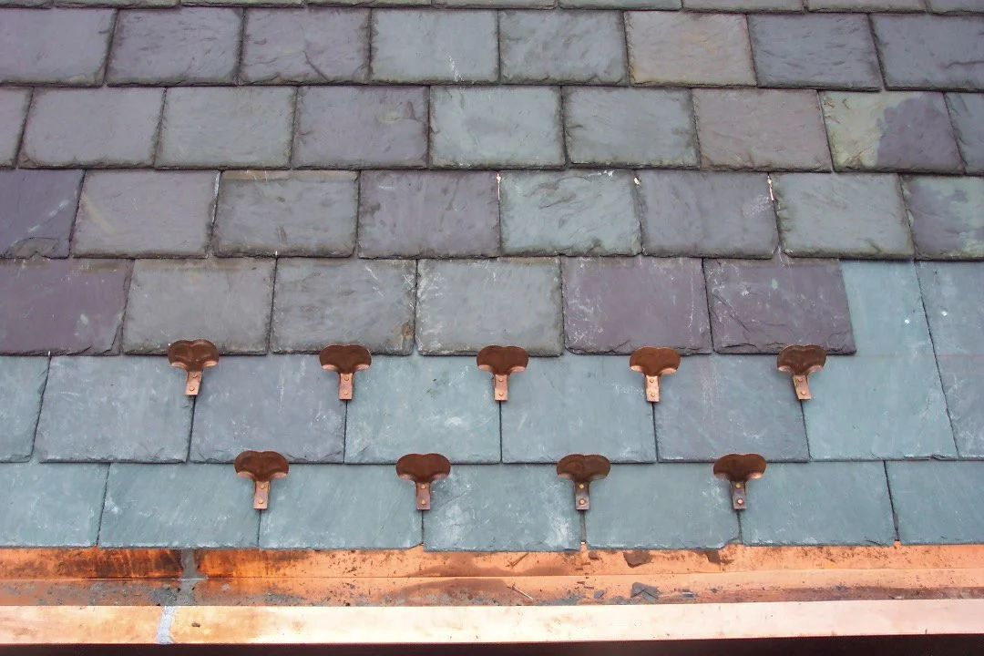 Close-up of slate roof shingles with several copper roofing nails arranged in a pattern.