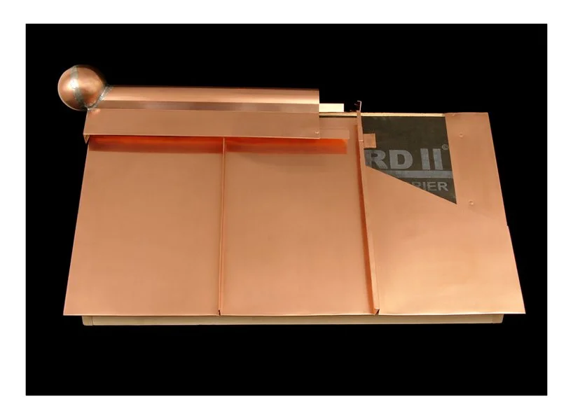 A copper-colored mechanical device with a metallic sphere on one end and various flat panels and components, possibly part of a scientific or industrial apparatus, on a black background.