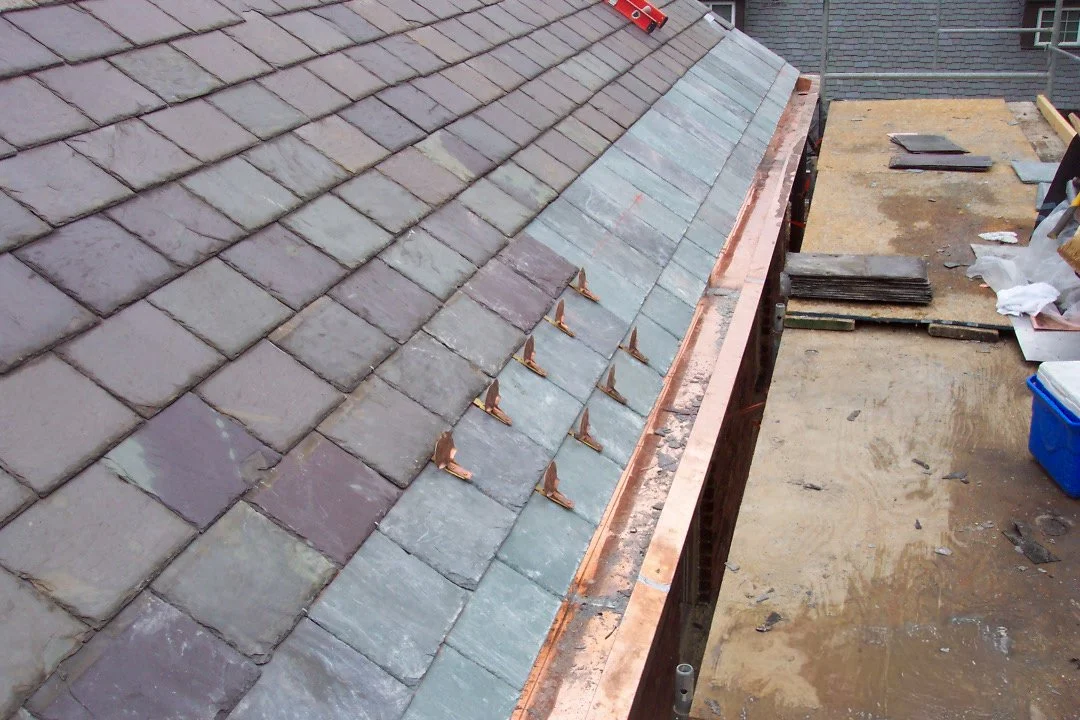A rooftop with slate tiles and copper flashing under construction, with work materials nearby.