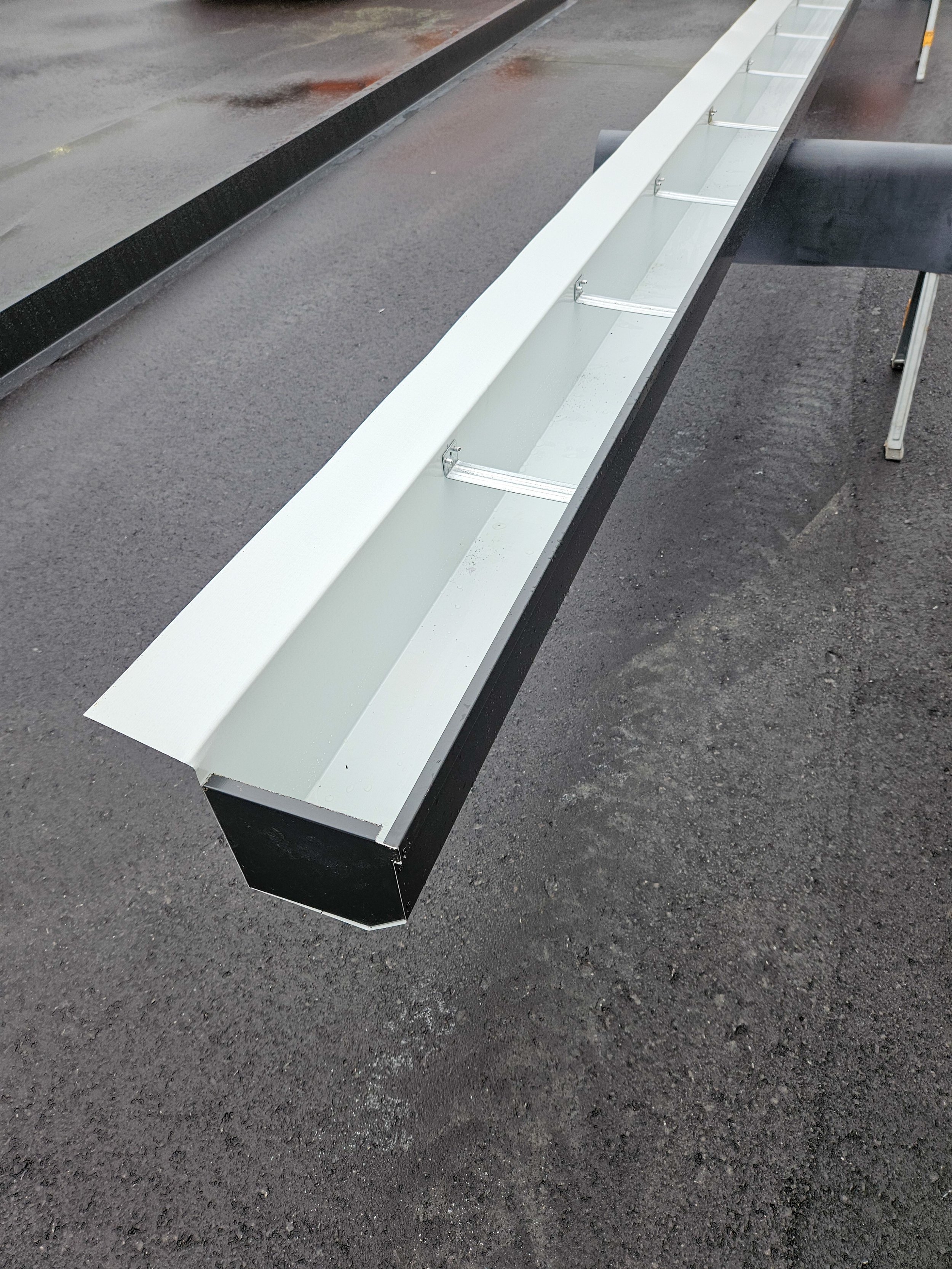 Metal gutter with brackets on a workbench outside, on a wet asphalt surface.