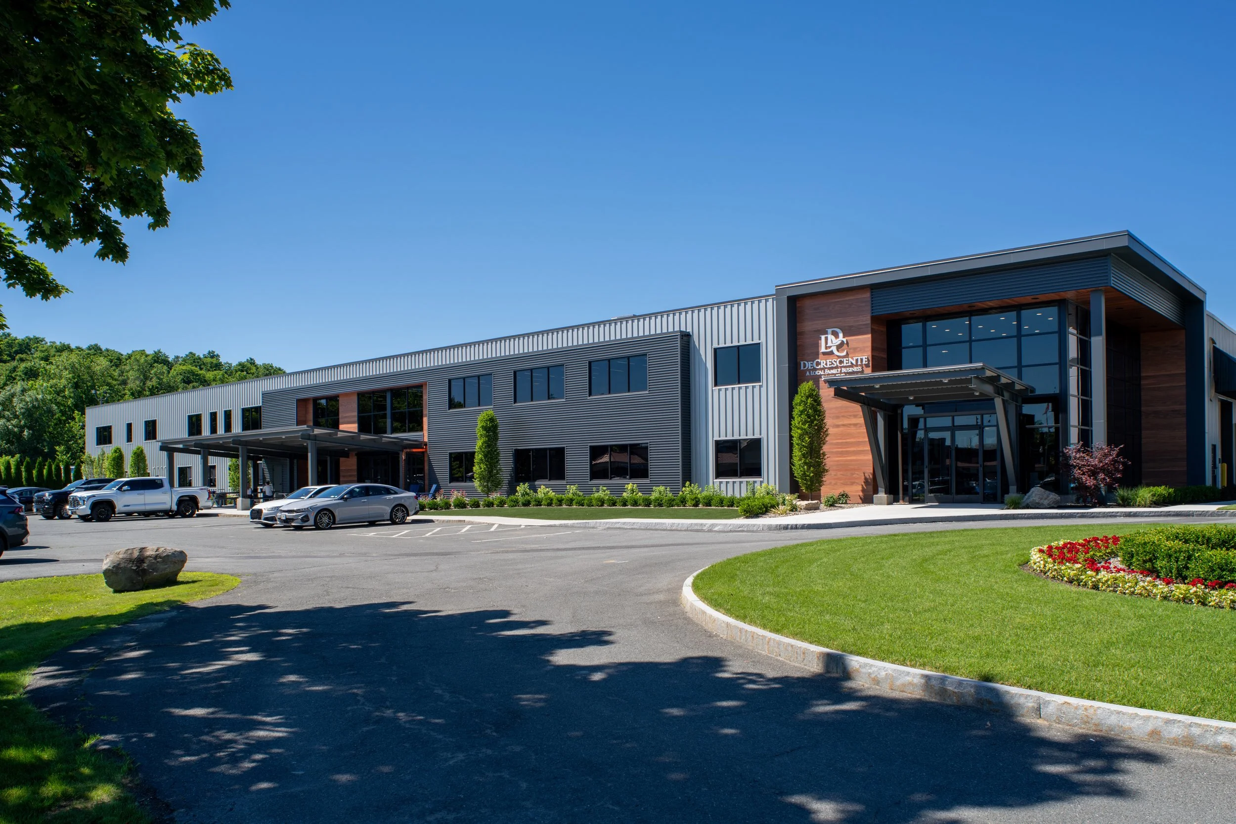 Modern commercial building with parking lot and landscaped lawn under a clear blue sky.