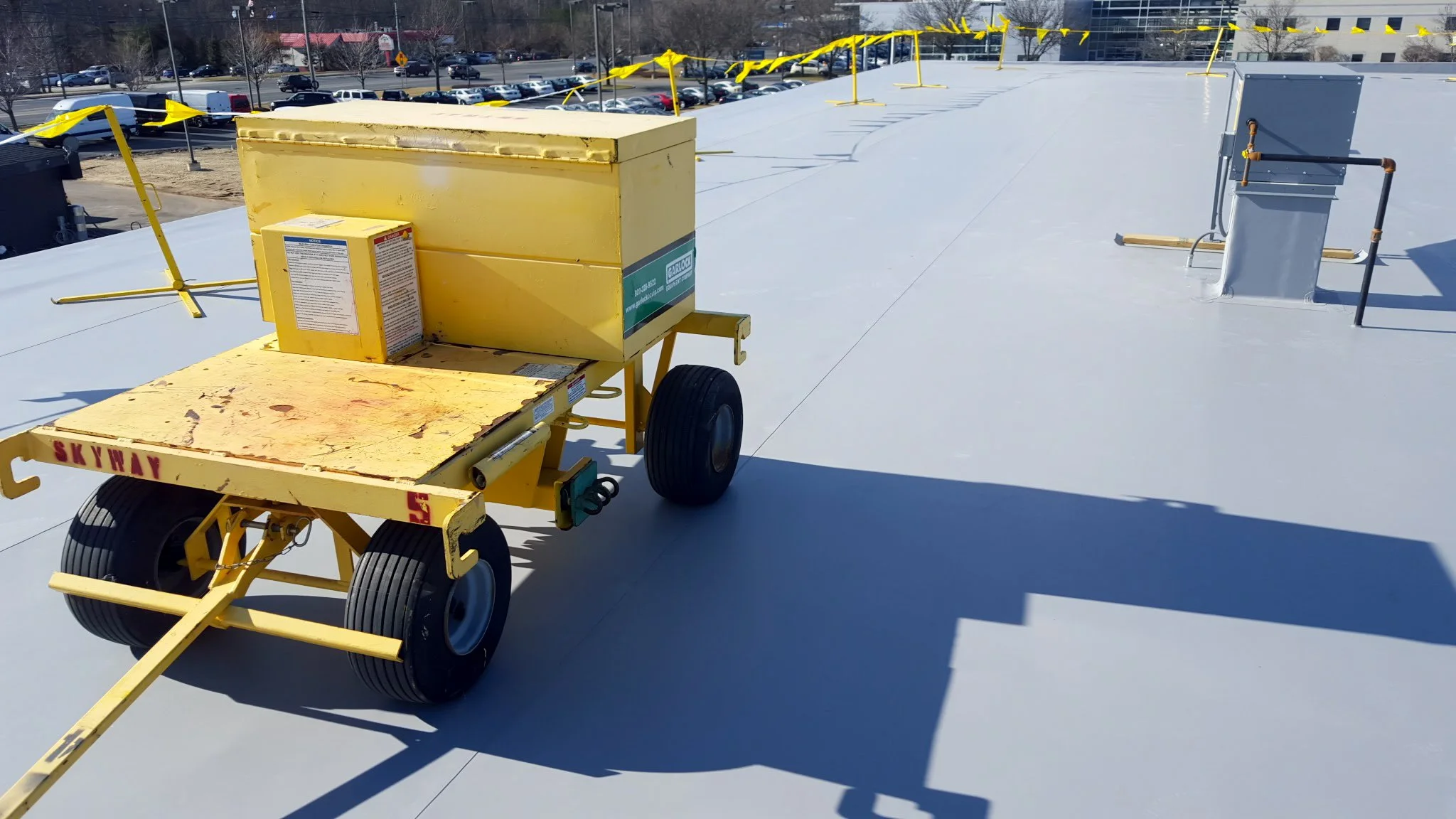 A yellow mobile lifting platform on a flat rooftop with parking lot and street in background.
