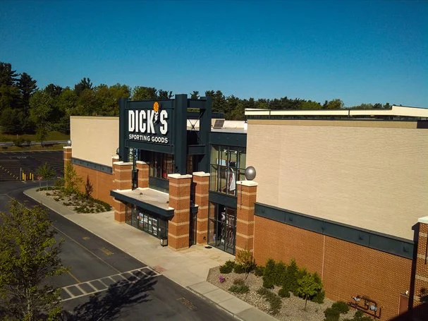 Exterior view of a Dick's Sporting Goods store with a large sign, brick accents, and a parking lot in front.