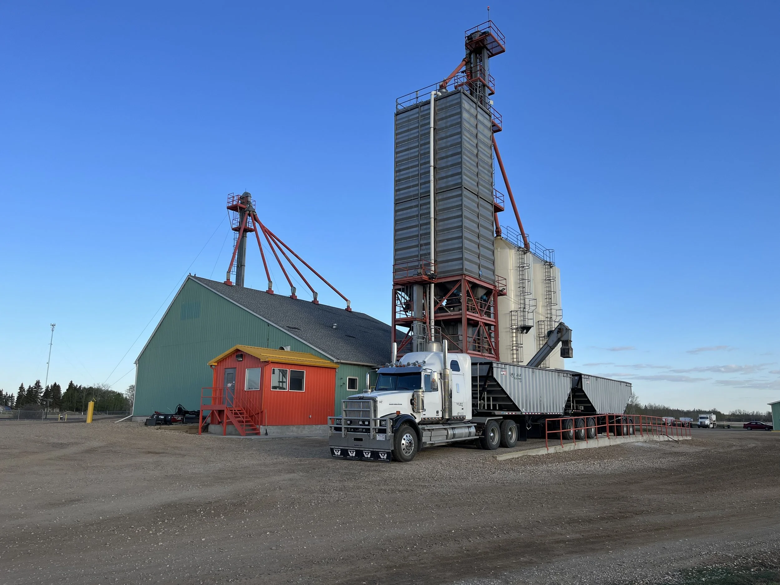 A large industrial grain elevator with a truck parked nearby, under a clear blue sky.