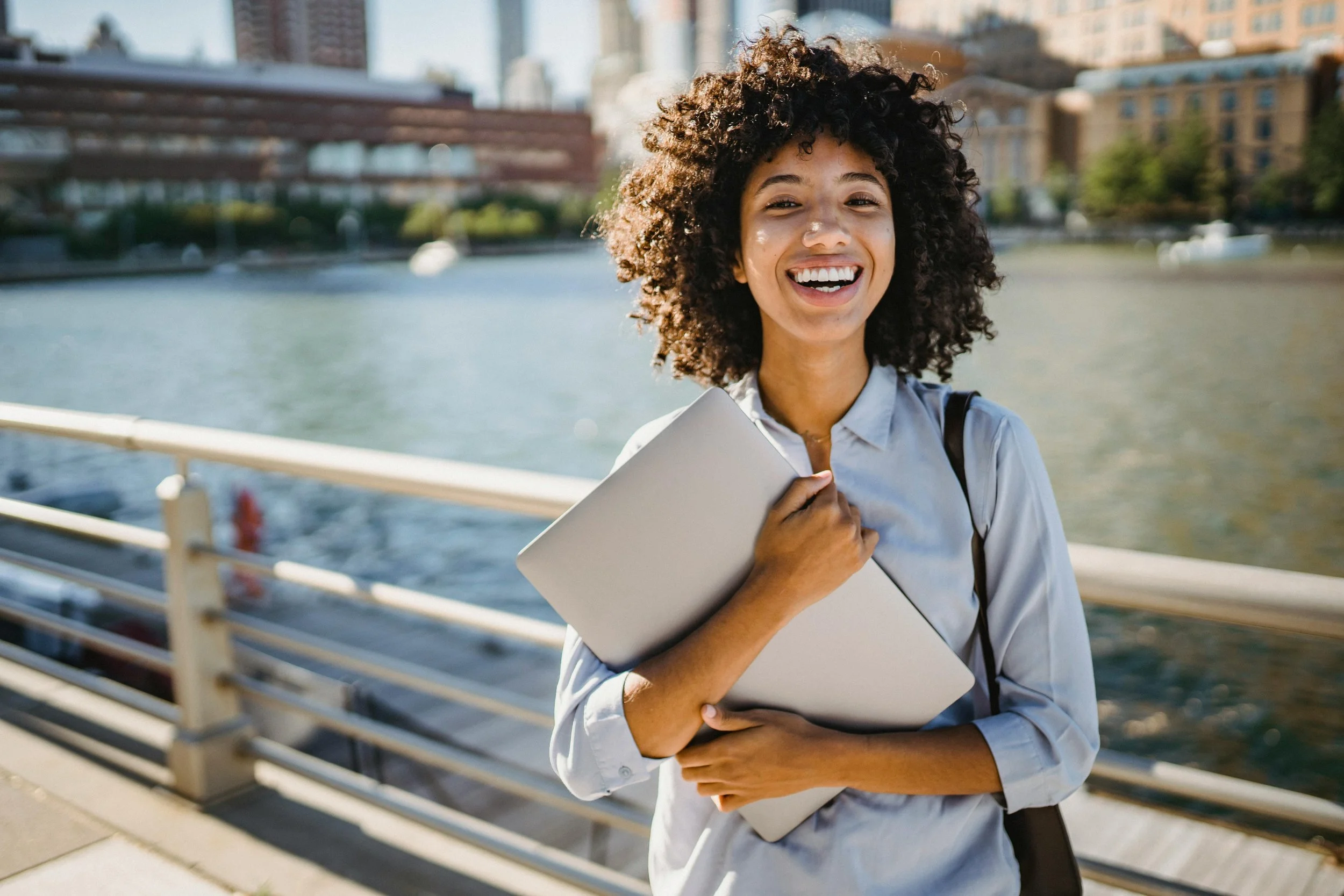 Smiling student holding a laptop by the waterfront