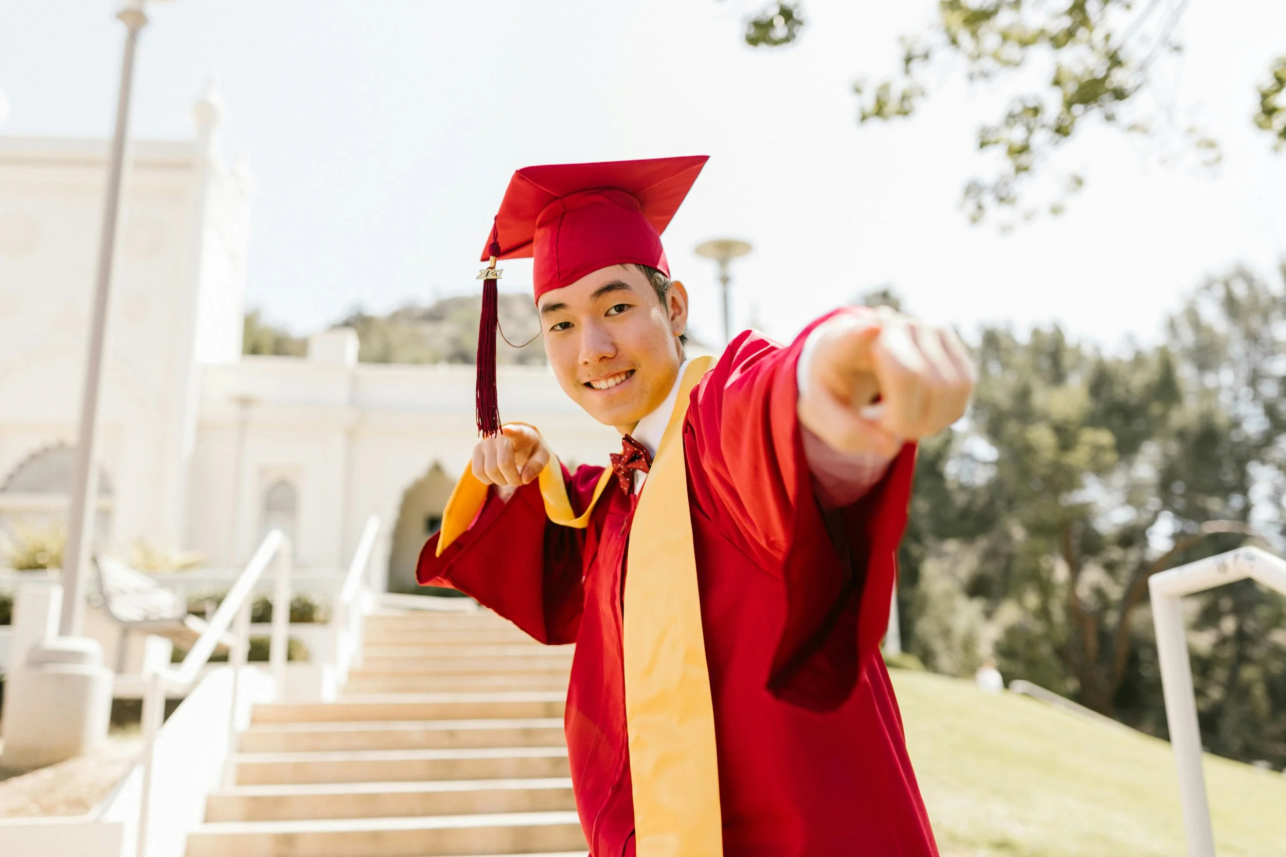 Graduate in a red gown pointing toward the camera