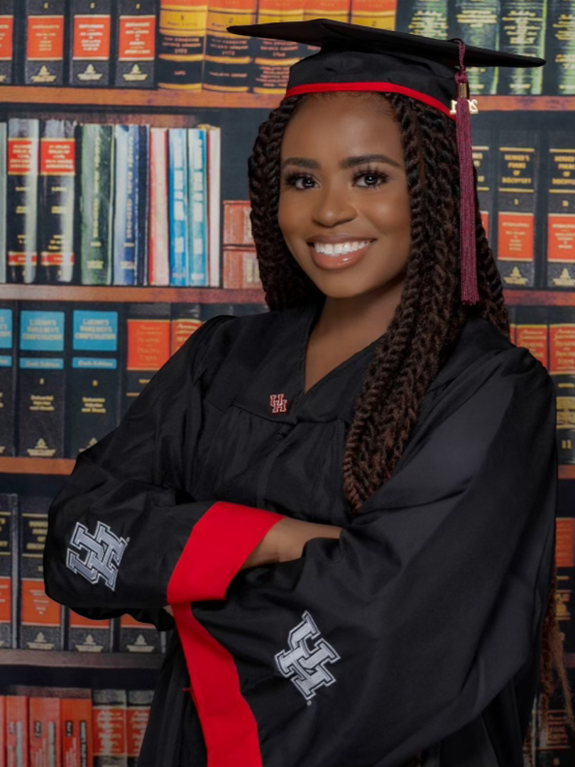 Last Mile awardee Jana J. in her graduation gown in front of library shelves